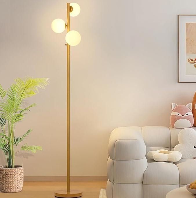 Interior design Inspiration featuring a stylish shoppable modern living room with a tall gold floor lamp with spherical white lights, a potted plant, a white cushioned sofa with plush toys, and wall art.