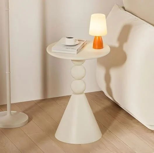 Living room design Inspiration featuring a stylish shoppable white bedside table with three spherical accents in the middle, holding a small lamp, a white cup, and some books, next to a bed with white bedding in a bedroom.