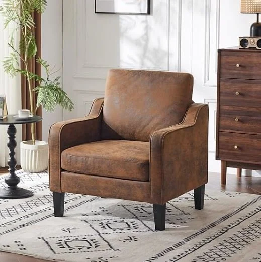rown leather armchair with wooden legs in a living room, next to a black side table with a small white vase and a white cup, and a wooden dresser with a lamp and radio on top, and a patterned rug on the floor. b