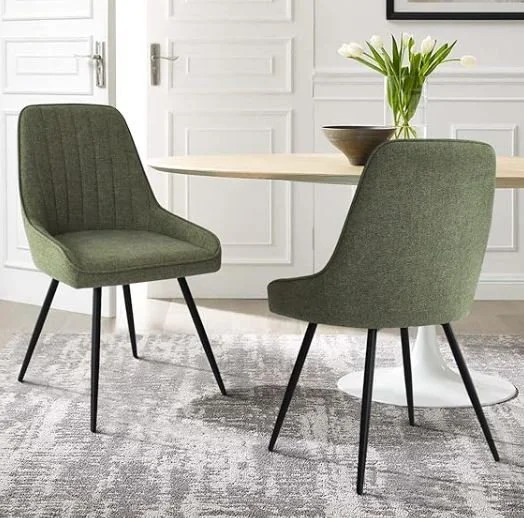 Dining room inspiration featuring a stylish shoppable green upholstered chairs around a round white table, a vase with white flowers on the table.