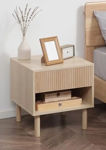 Light wood nightstand with two drawers and open shelf, decorated with a white vase of lavender, a picture frame, and a small clock, next to a bed.