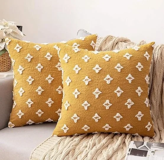 Living room design Inspiration featuring a stylish shoppable  mustard yellow decorative pillows with white floral patterns on a white couch, with a beige knitted blanket and a magazine nearby.