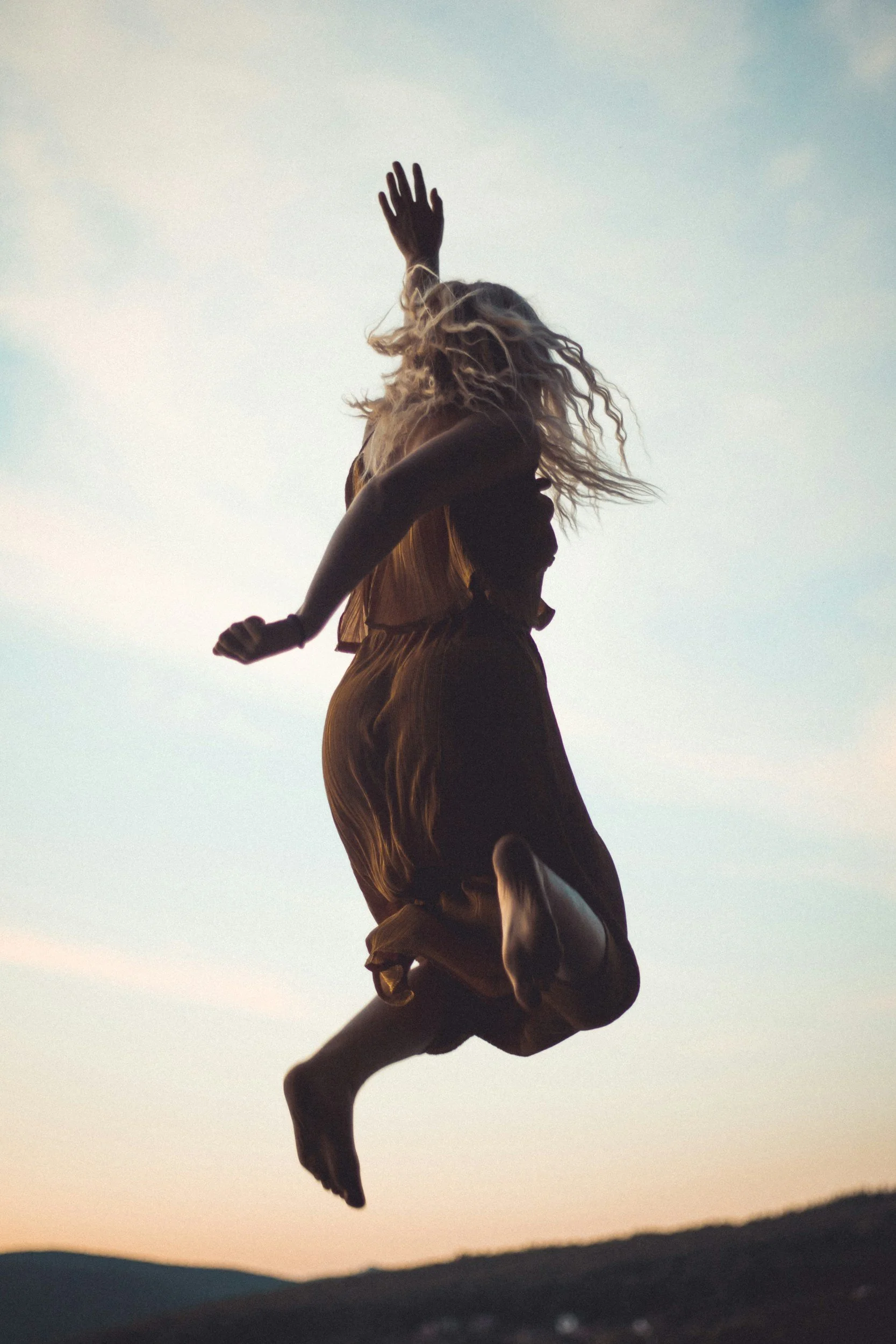 An image depicting someone experiencing joy and elation related to therapy and finding the right space to meet their therapist. The person is jumping in the air at sunset or sunrise, with hills in the background.