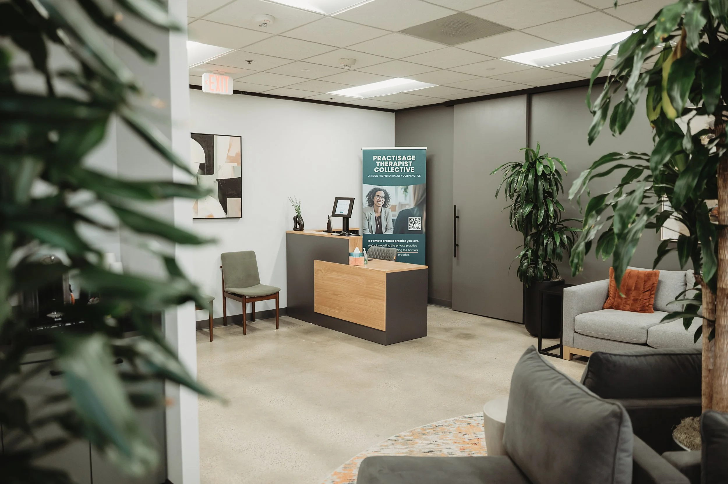 A waiting area inside the office of Daylily Therapy. It features a reception desk, a banner that reads 'Practisage Therapist Collective.'