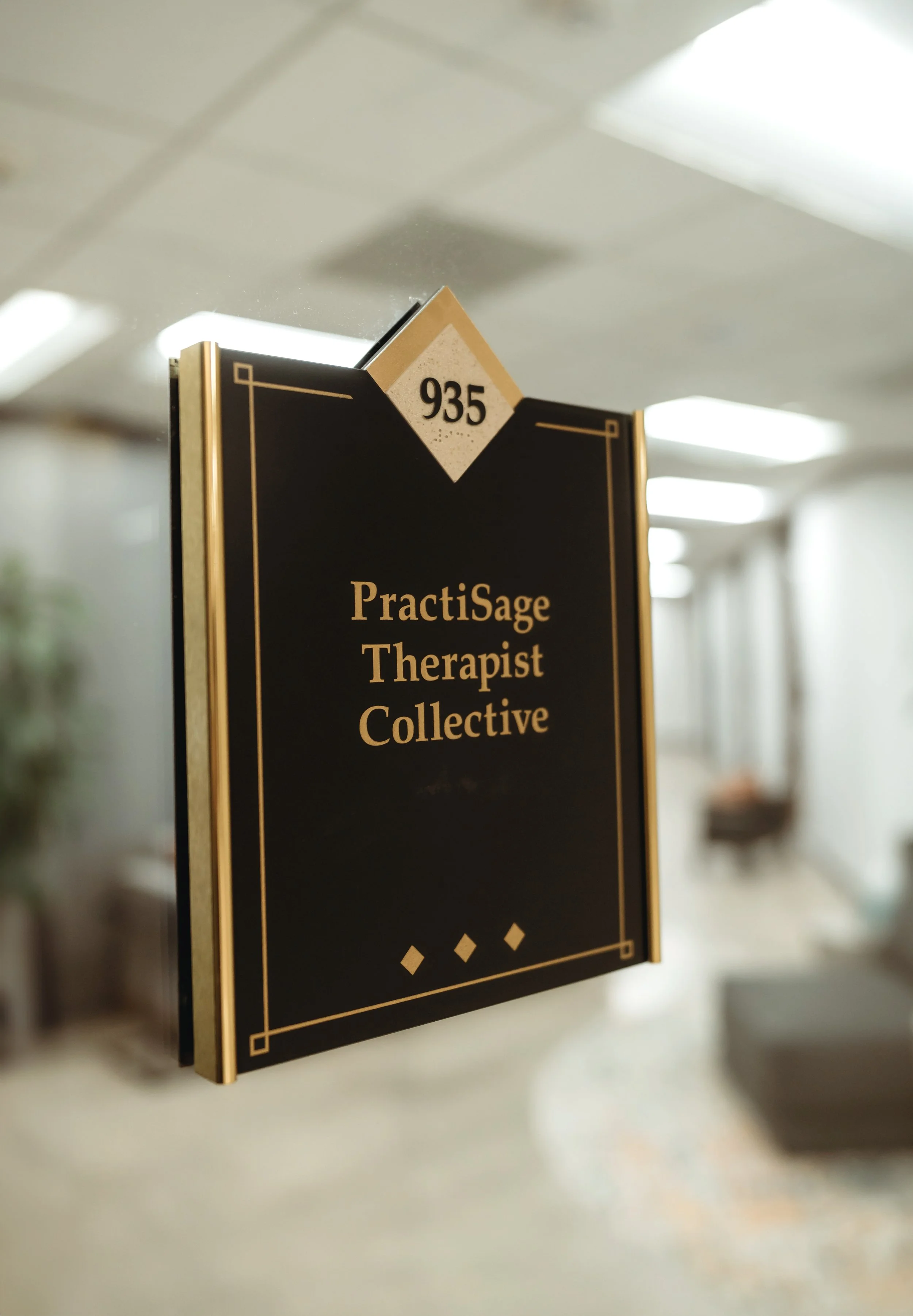 Black and gold framed sign with the number 935 at the top, and text reading 'PractiSage Therapist Collective' below. This is where the office of Daylily Therapy is located.