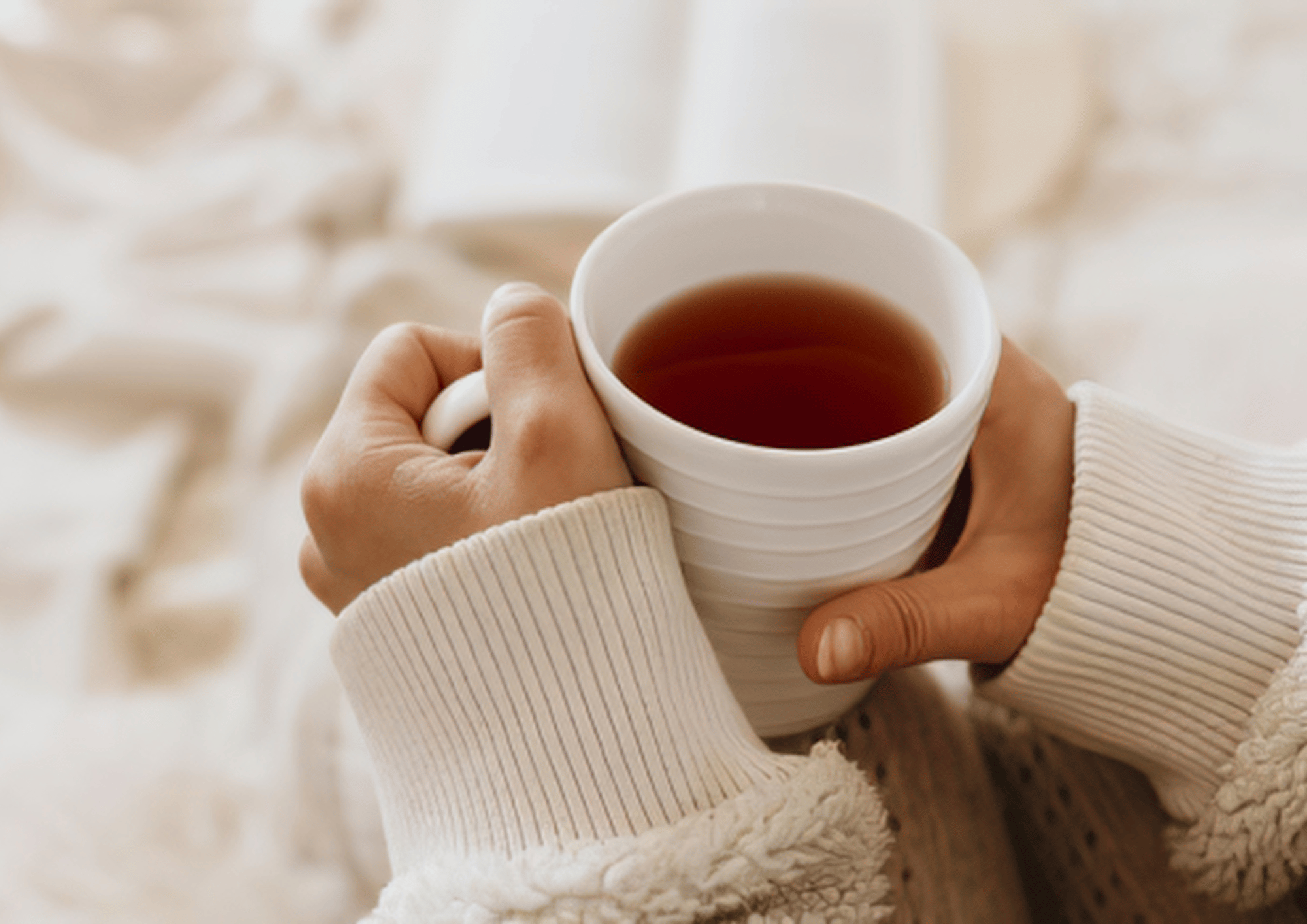 A person holding a white striped mug filled with tea, wearing cream-colored sweater sleeves with lace trim. Depicting calm and comfort in a therapy space.