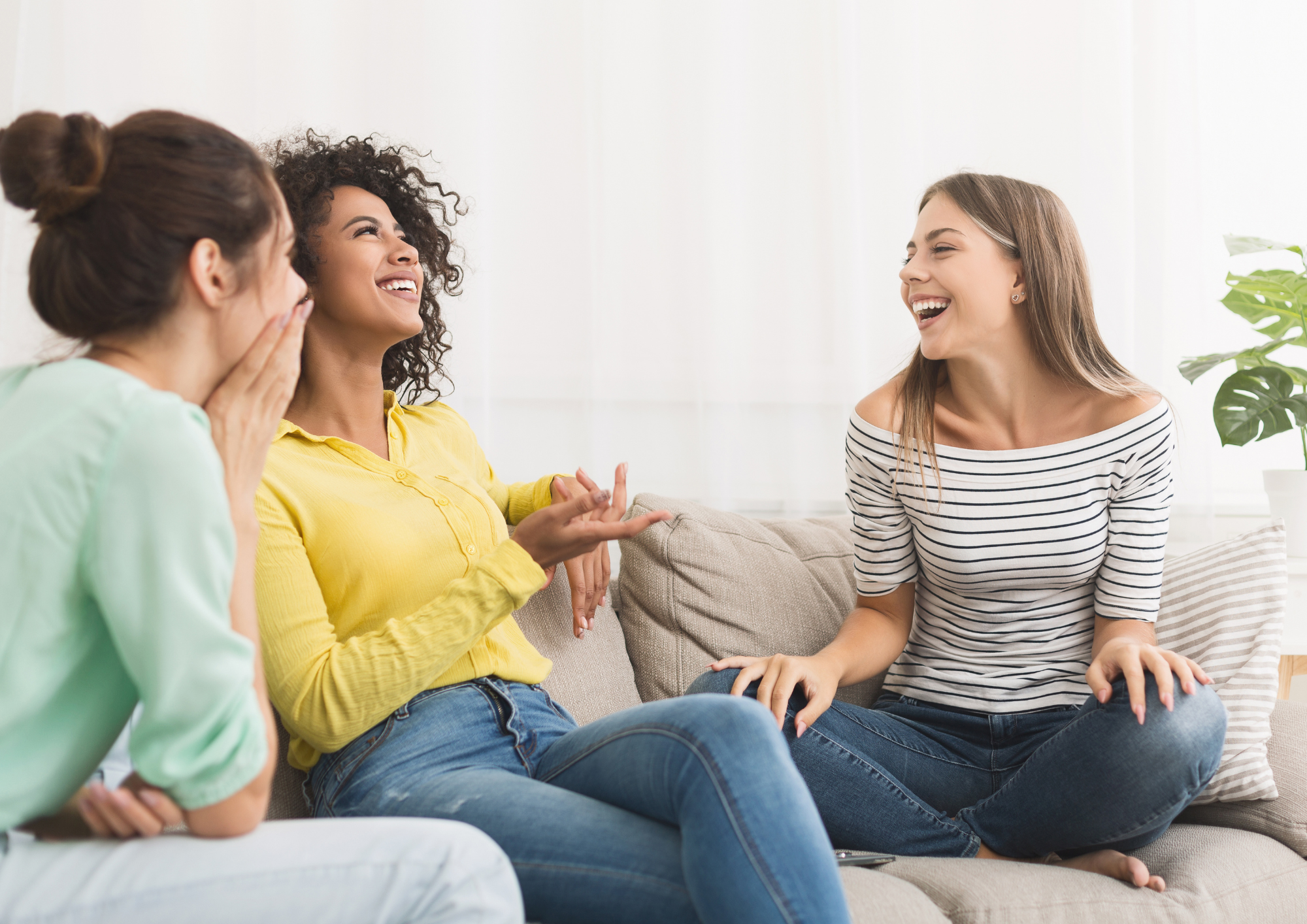 Three people sitting together on a comfortable couch sharing a warm, genuine laugh during a lighthearted moment.