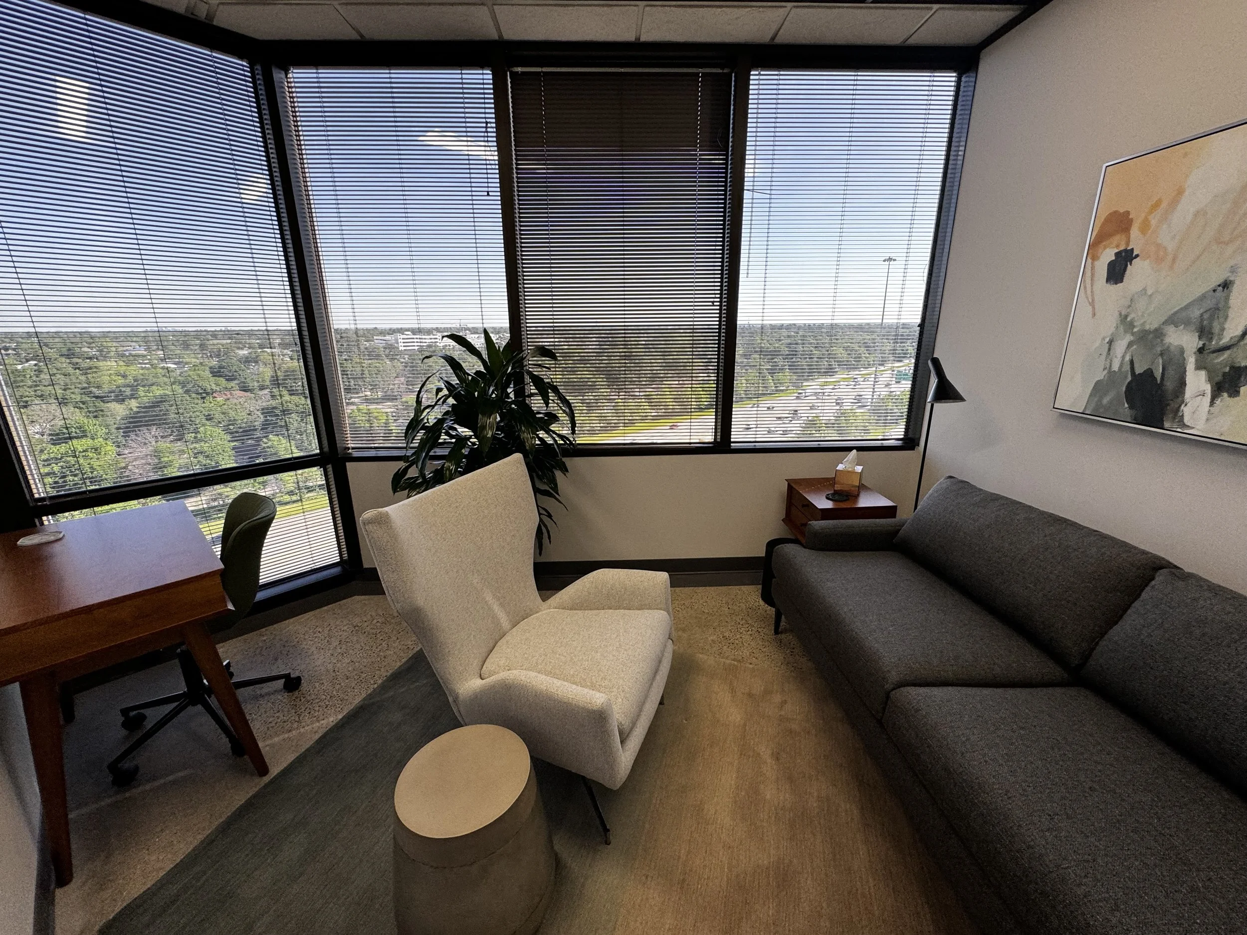 A private therapy office in The Heights, Houston. The space is utilized by Daylily Therapy, it includes a dark grey couch, light grey arm chair, and desk.