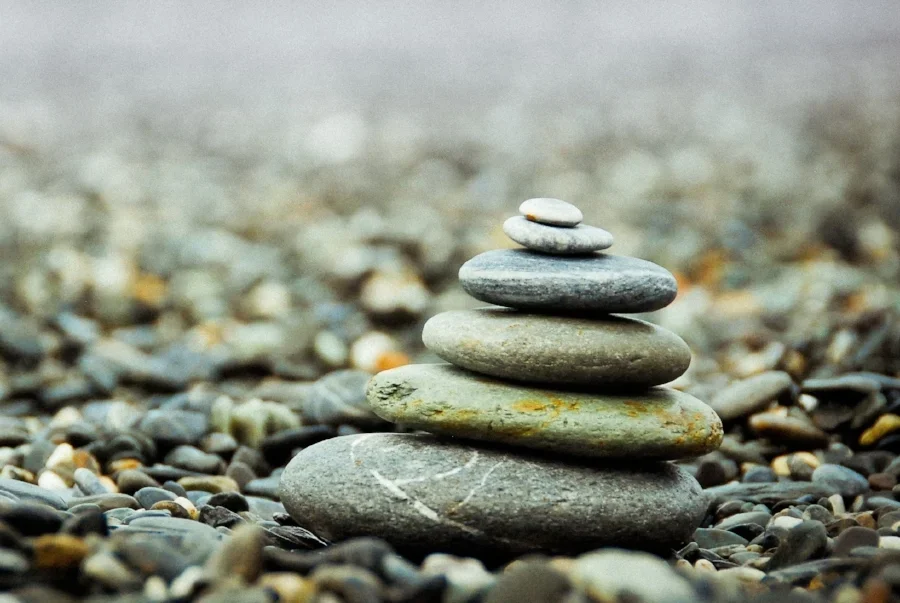 A stack of six smooth, flat stones, balanced on a pebble-covered beach, with a blurred beach background.