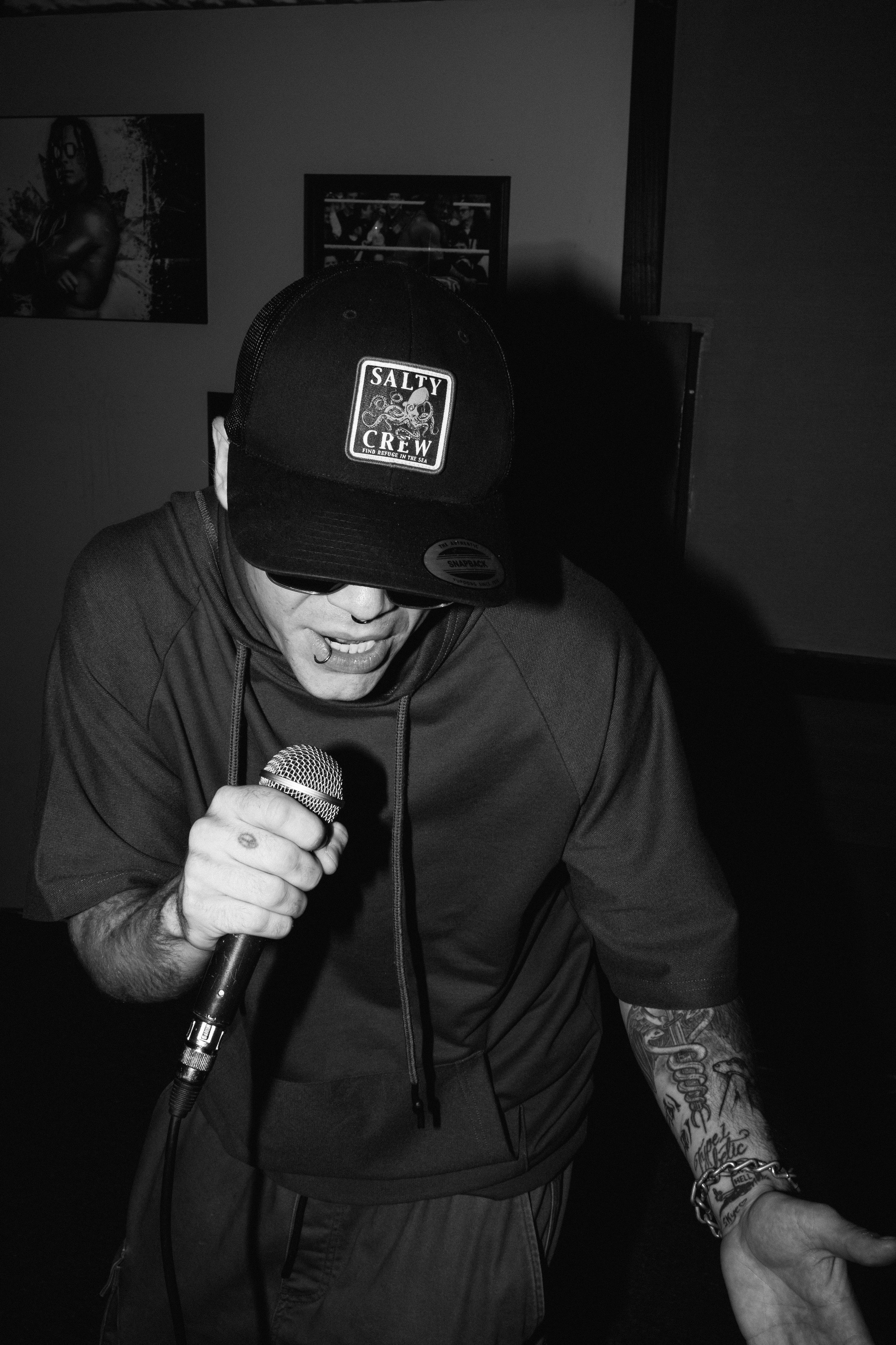 FAYD Music Performance Photo. wearing a Salty Crew cap, sunglasses, and a hoodie holding a microphone while performing or speaking.