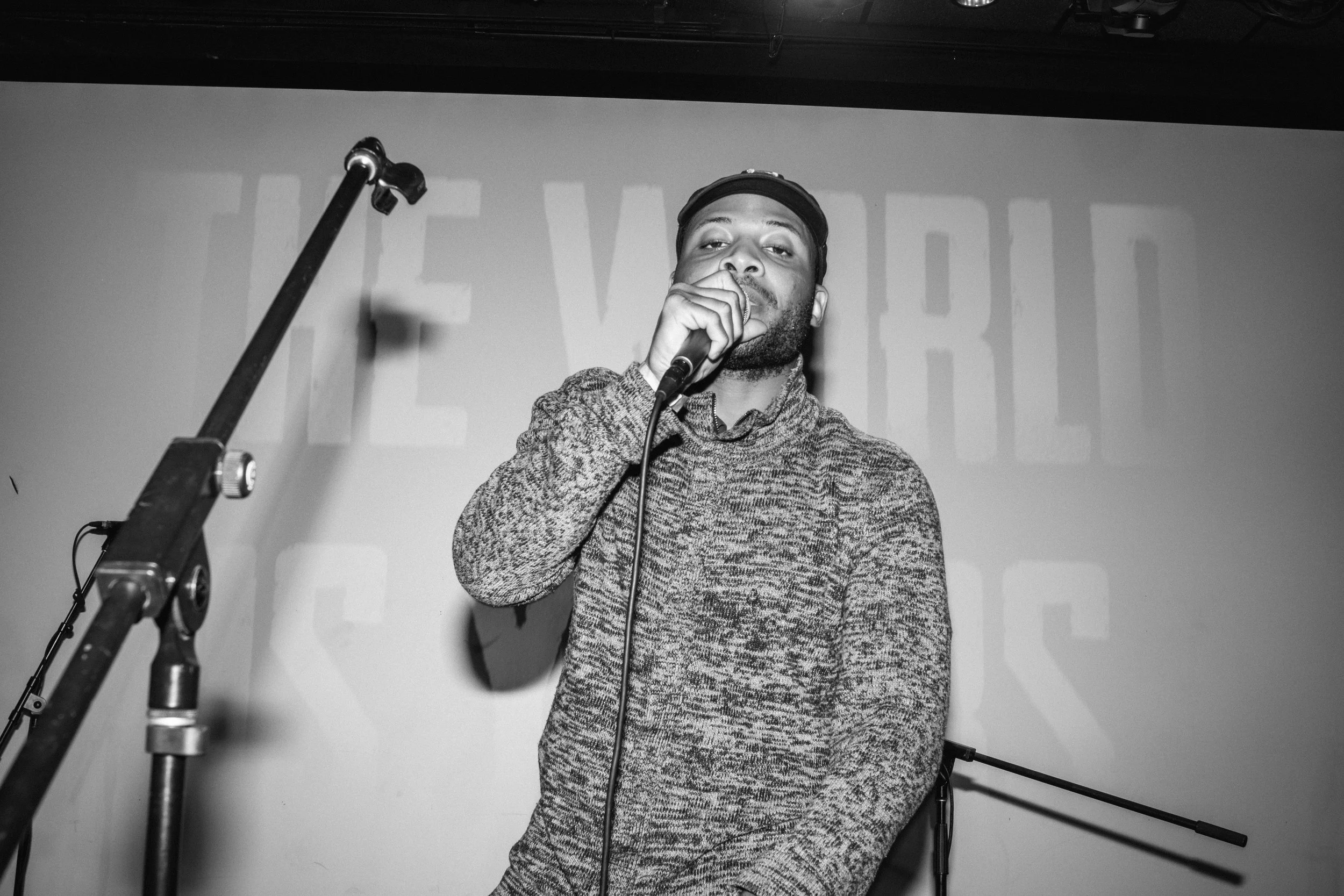 Polo Sho on stage holding a microphone on stage in front of a large screen with partially visible text.