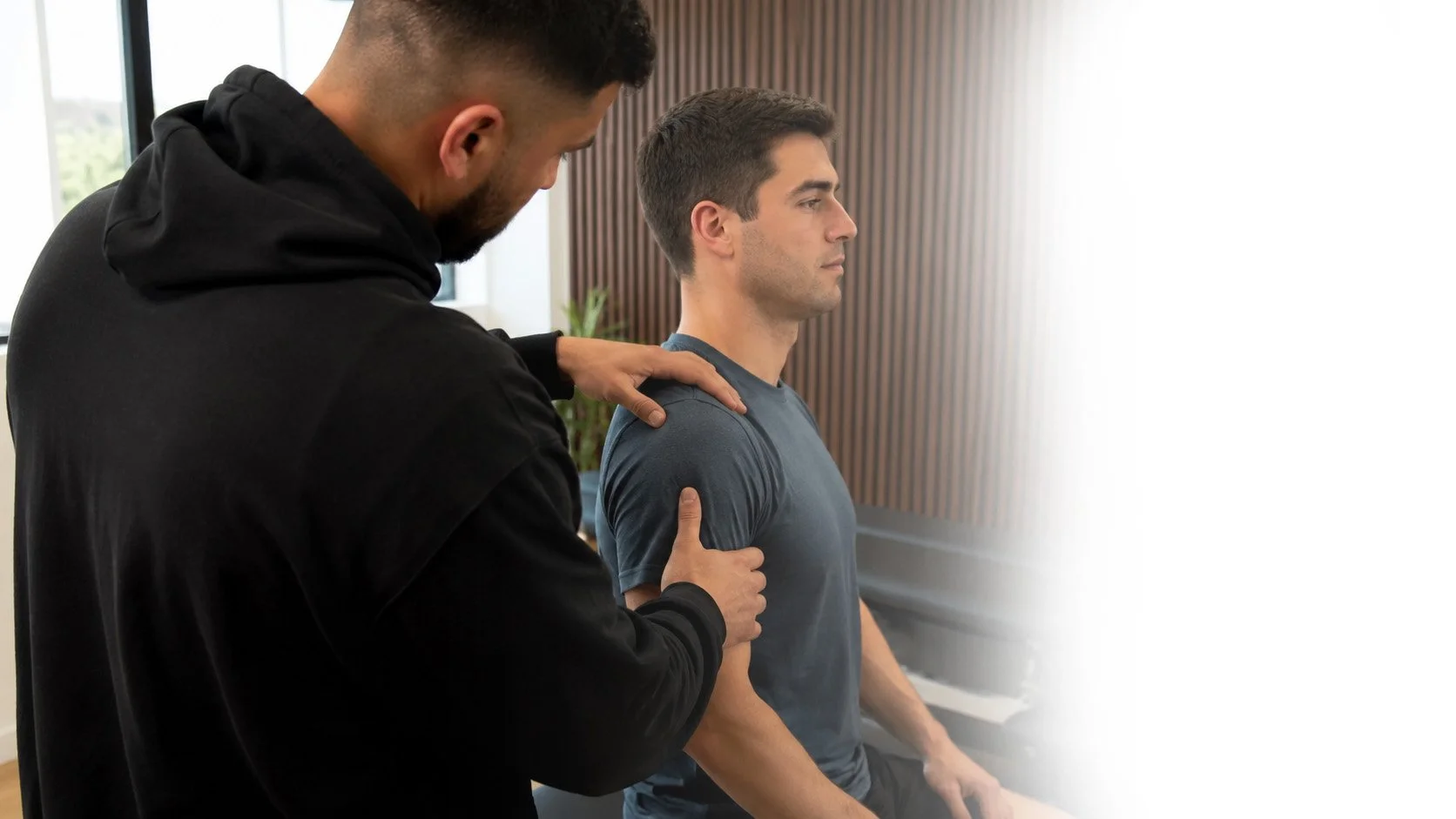 Chiropractor assessing a seated patient's shoulder and upper arm at Back In Sync in New Malden