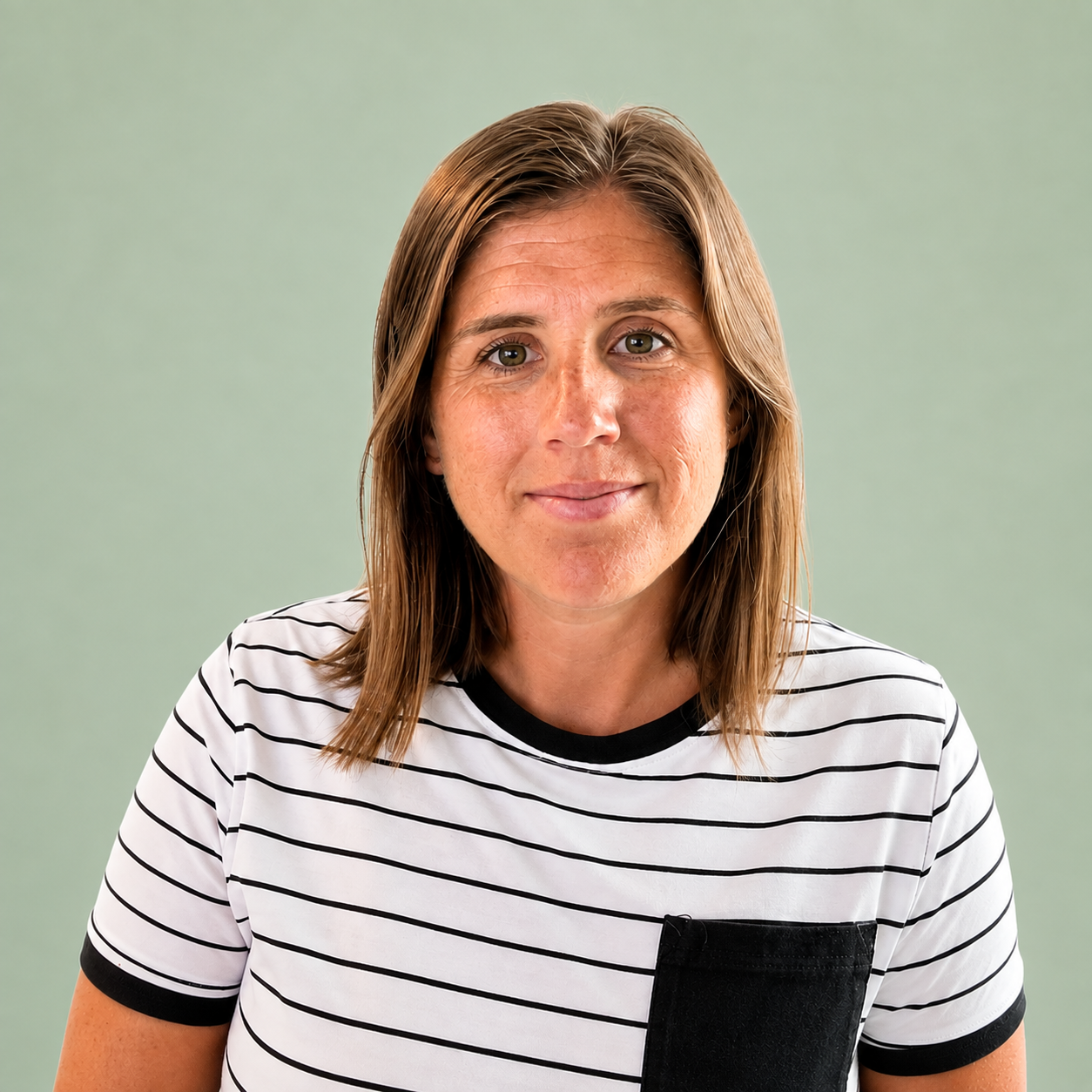 A woman with shoulder-length brown hair , smiling, wearing a white T-shirt with black horizontal stripes and a black pocket on the left side, against a light green background.