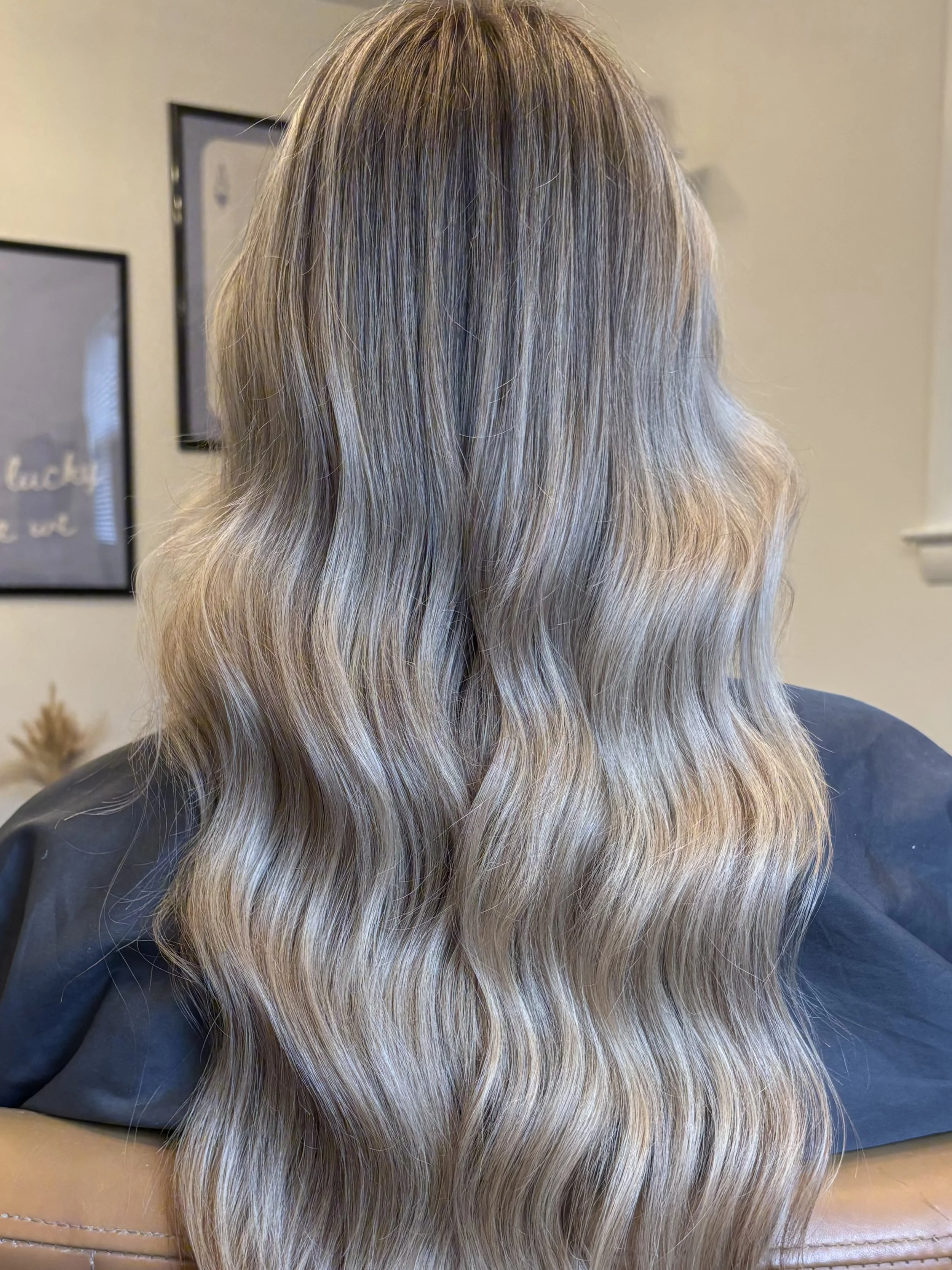 Back view of a woman with long wavy blonde hair in a salon chair.