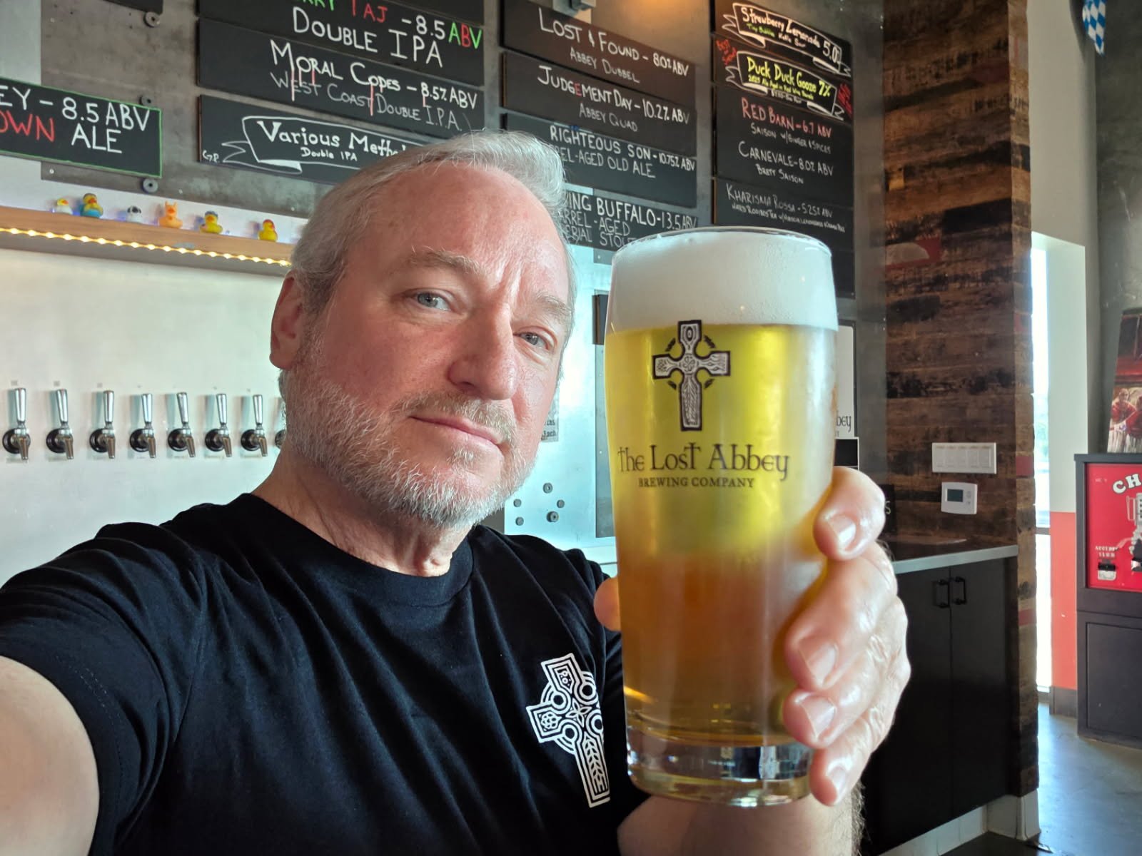 Person in a hoodie with hood up and hands together in prayer position, surrounded by shelves of bottles in a dimly lit setting.