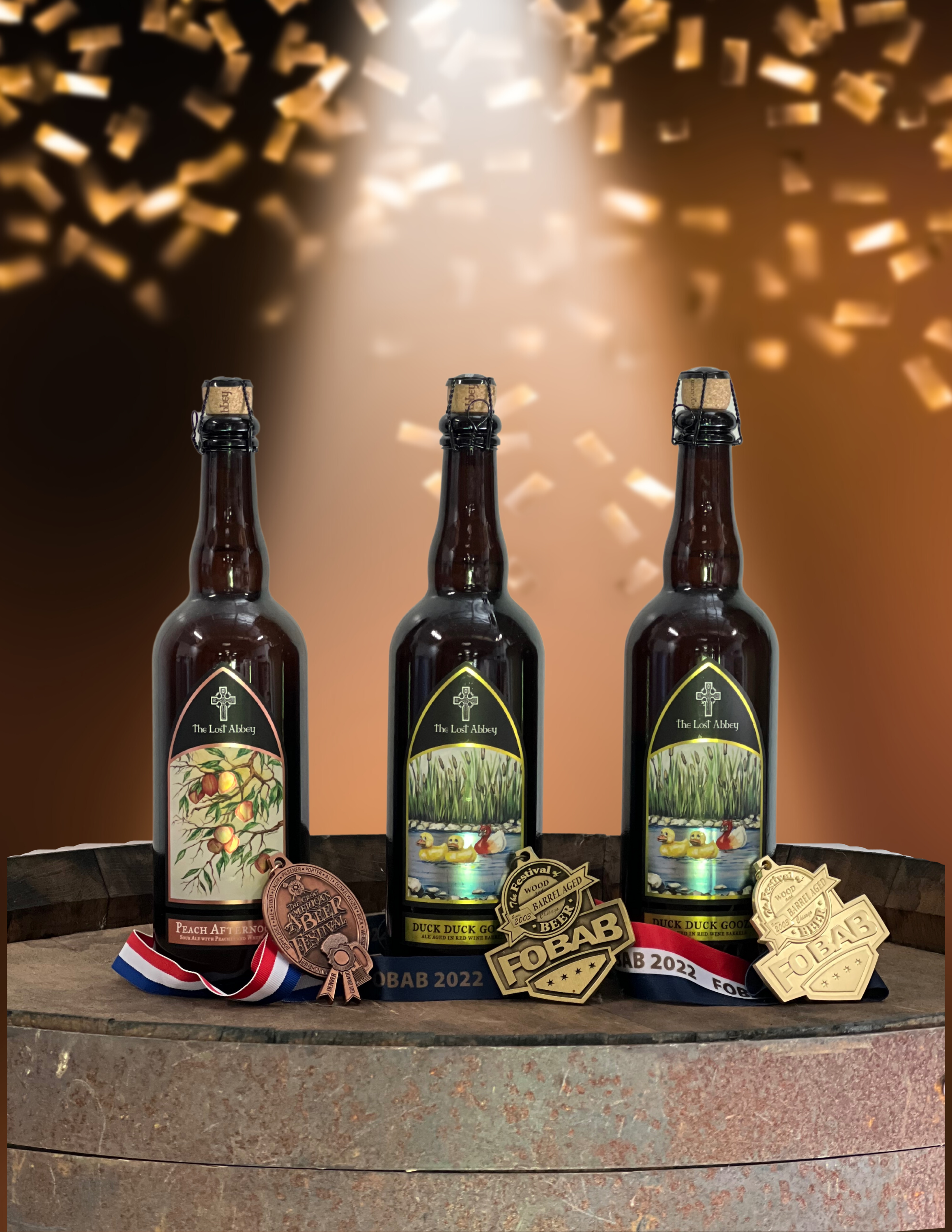 Three bottles of beer labeled 'The Lost Abbey' with medals and ribbons in front, set on a wooden barrel with a background of falling confetti and warm lighting.