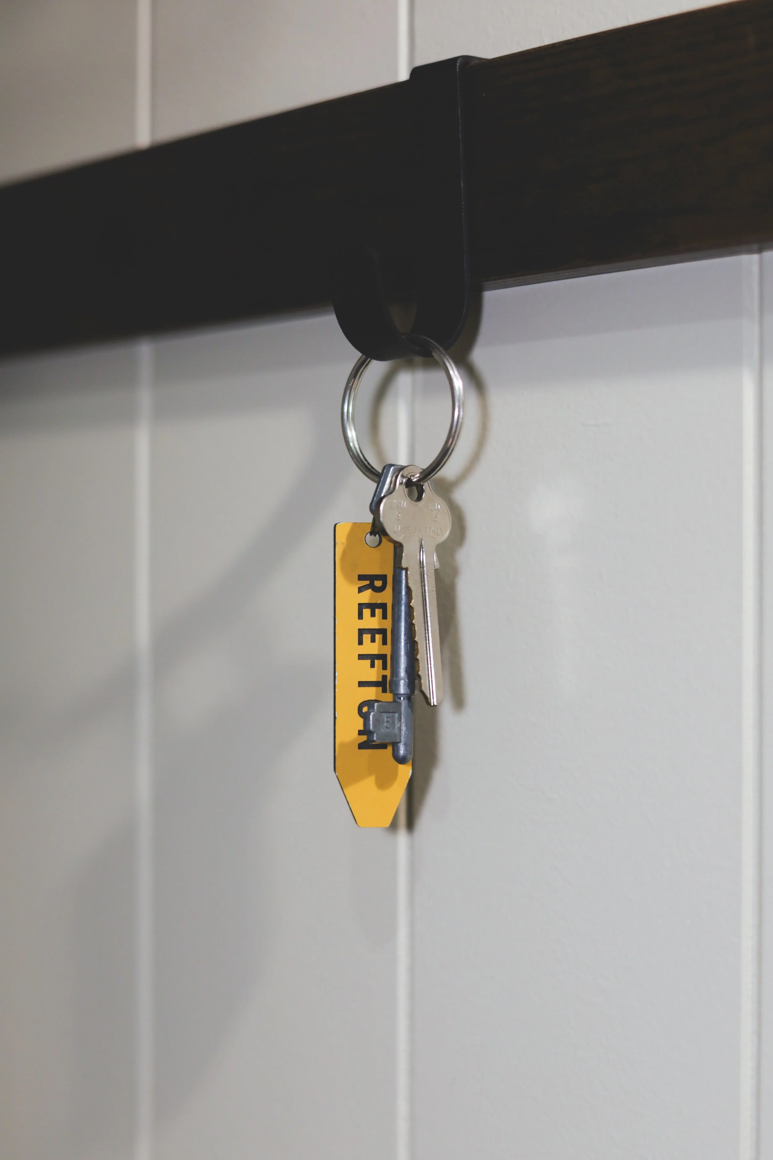 Key attached to a black hook on a dark wooden shelf, with a yellow keytag reading 'RESTRICTED' hanging below.