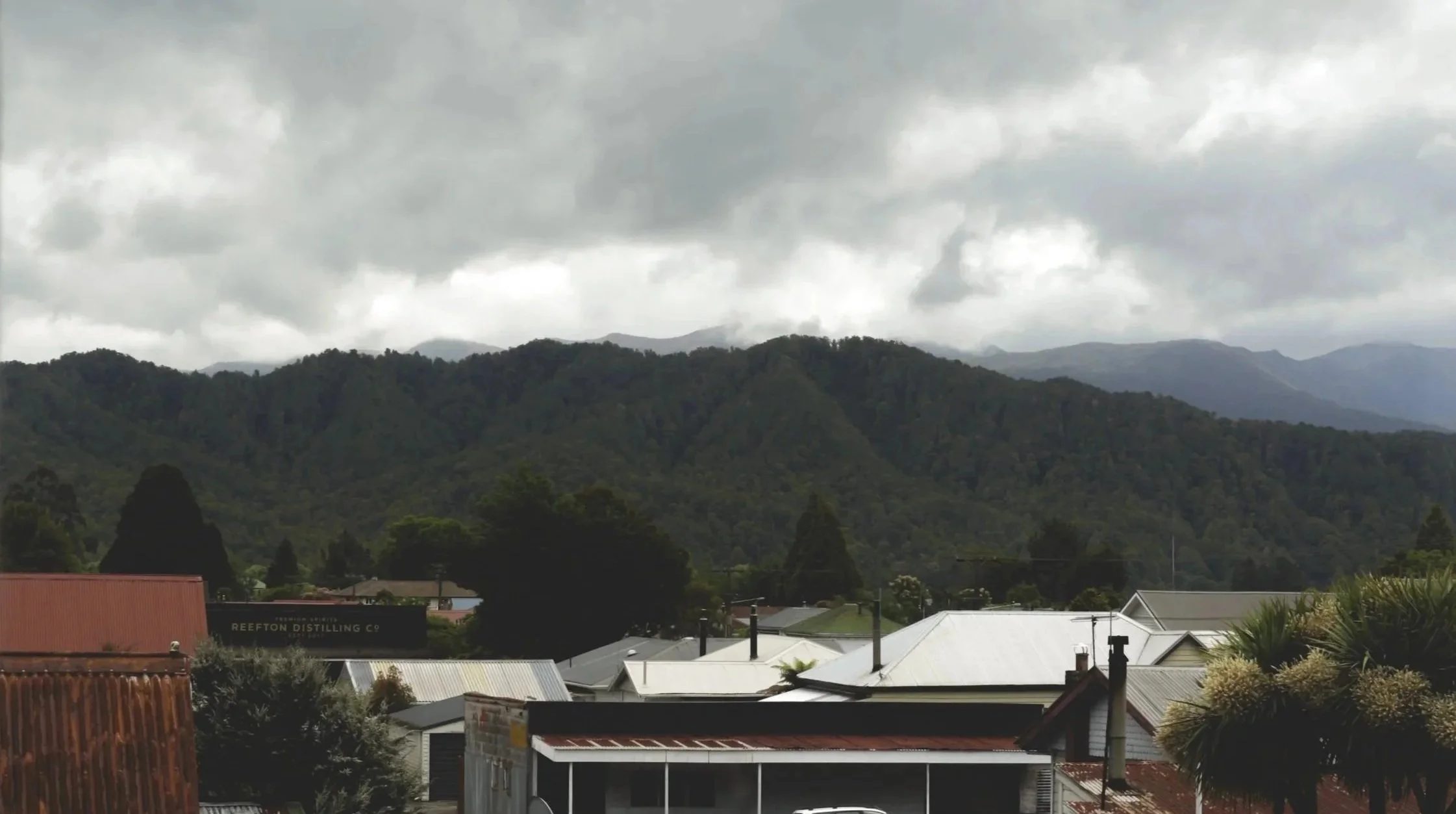 Overcast sky over a small town with mountains in the background, rooftops, and trees.