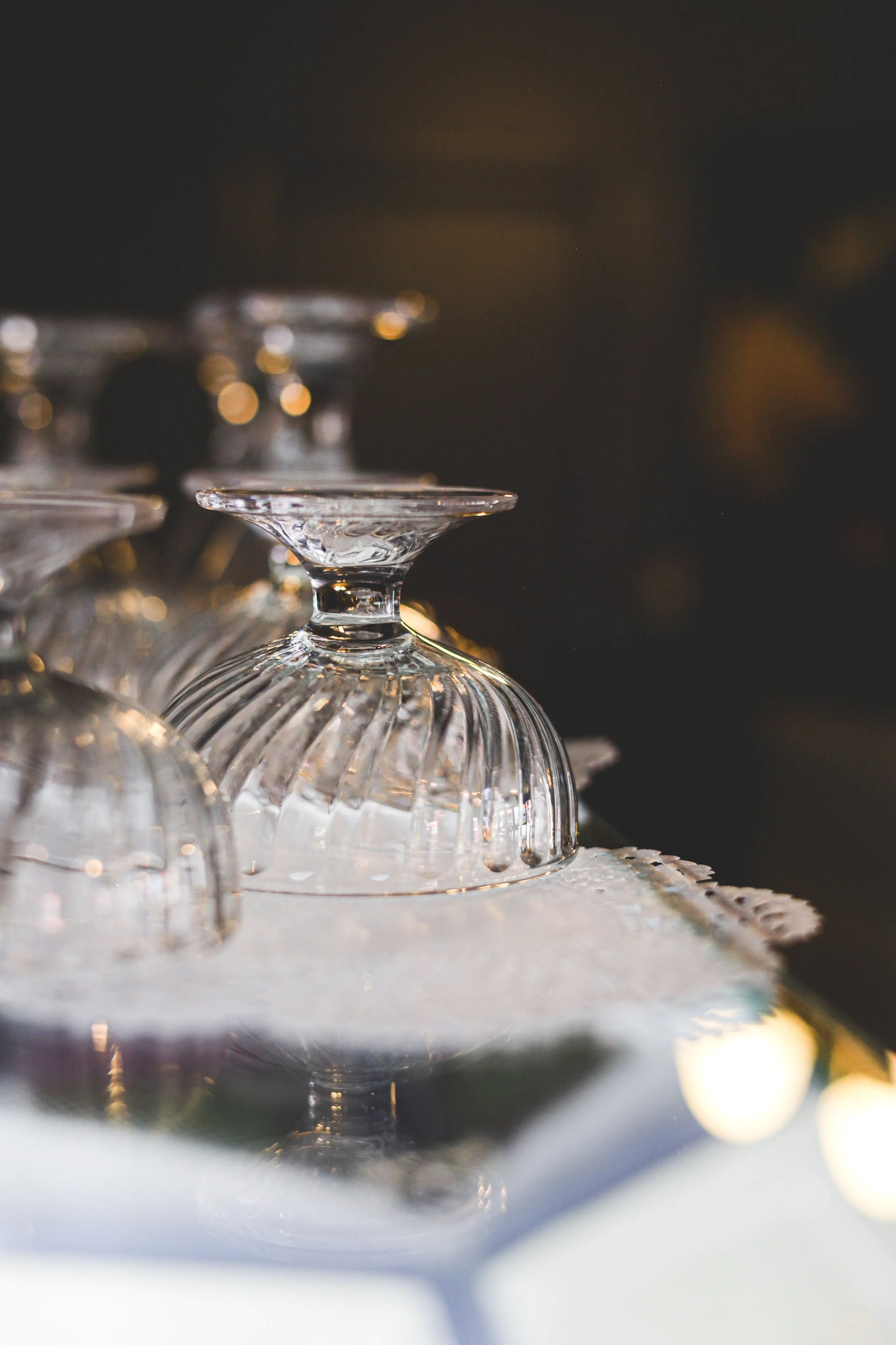 Upside-down glassware displayed on a table, with a dark background and warm lighting reflections.