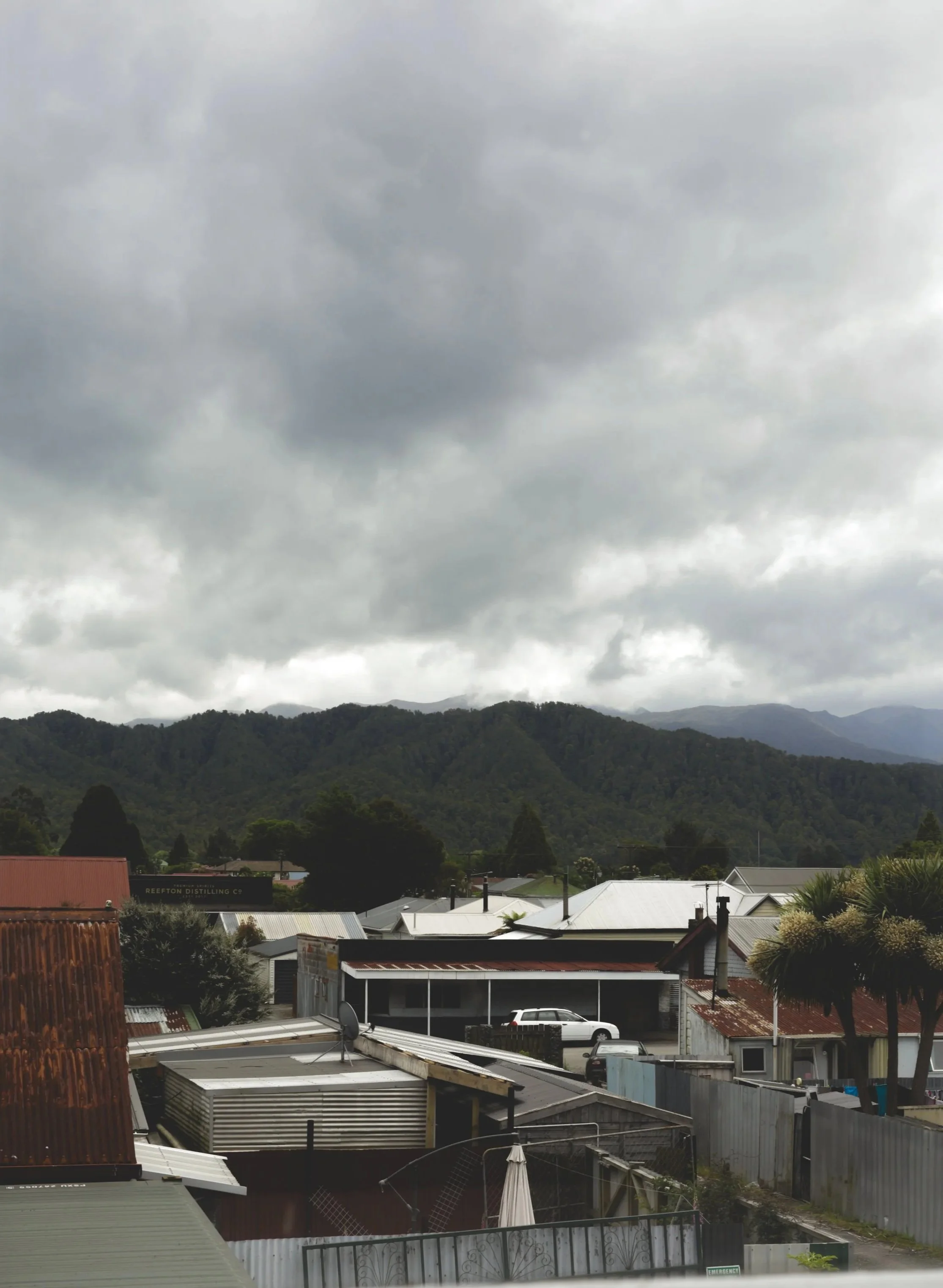 Overcast sky above a small town with houses and trees, mountains in the background.