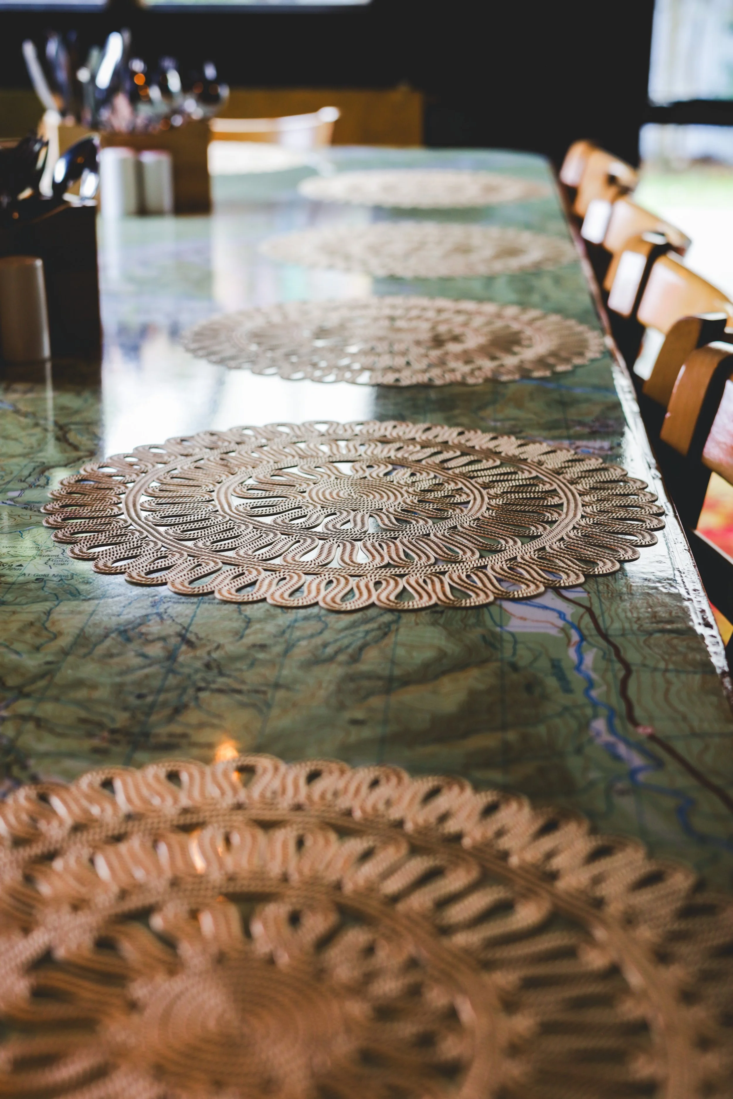 A long wooden dining table with intricately designed round woven placemats arranged along its length.