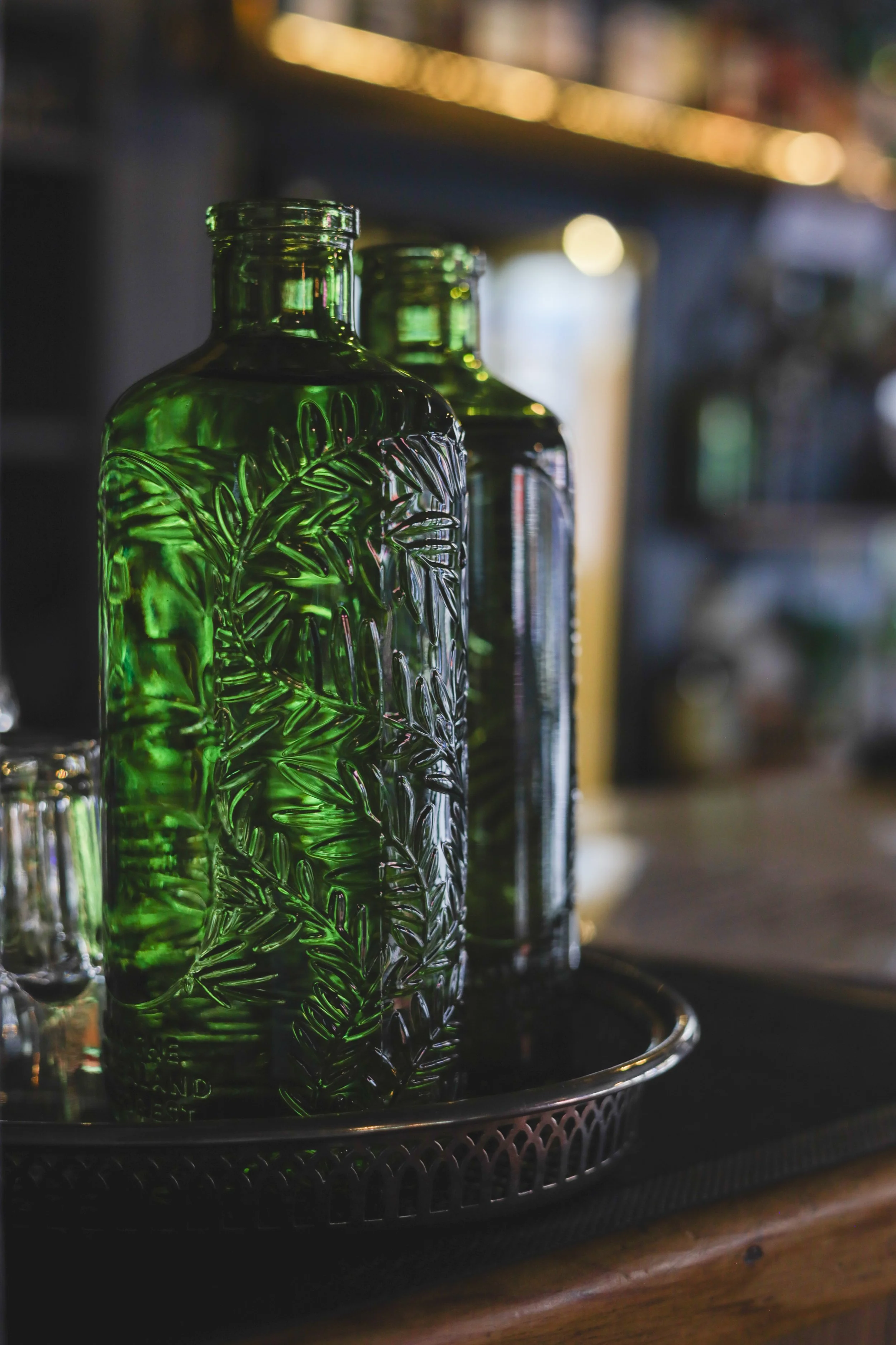 Green glass bottles with embossed leaf patterns placed on a black tray.