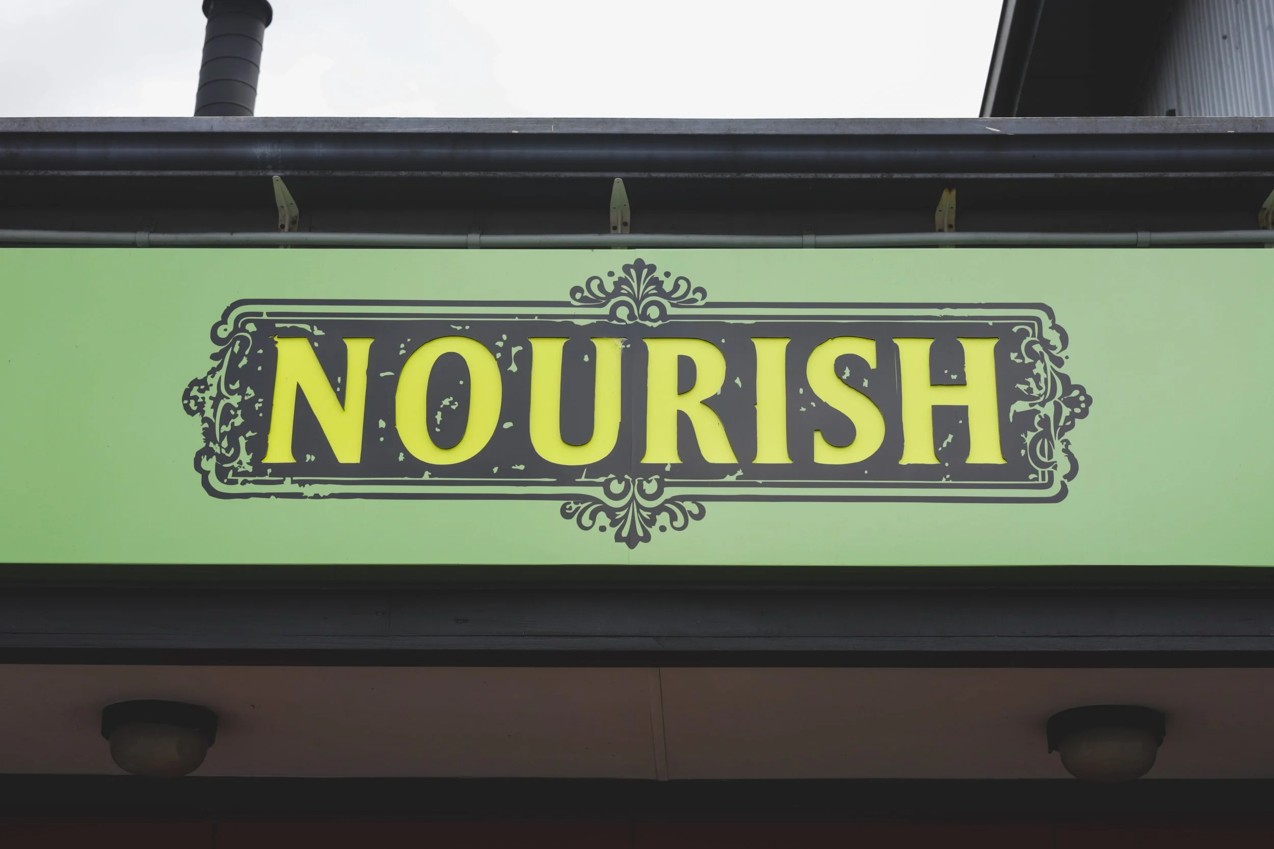 Sign with the word 'NOURISH' in bold yellow letters on a green background.