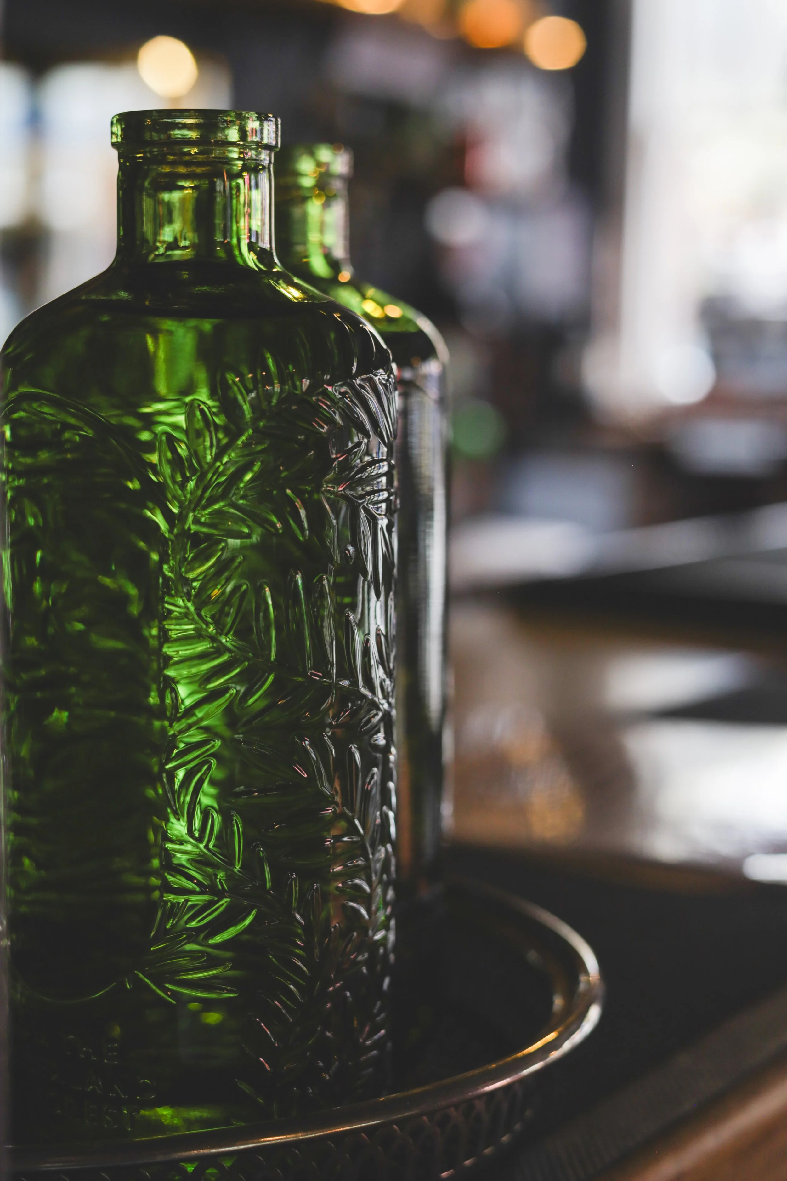 Two green glass bottles with embossed tropical leaf patterns on a bar or countertop.