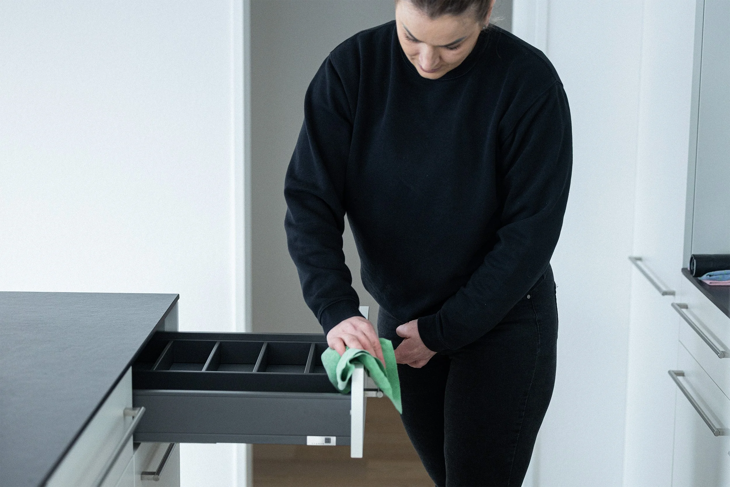 Frau beim Aufziehen einer Küchenschublade mit einem grünen Tuch.