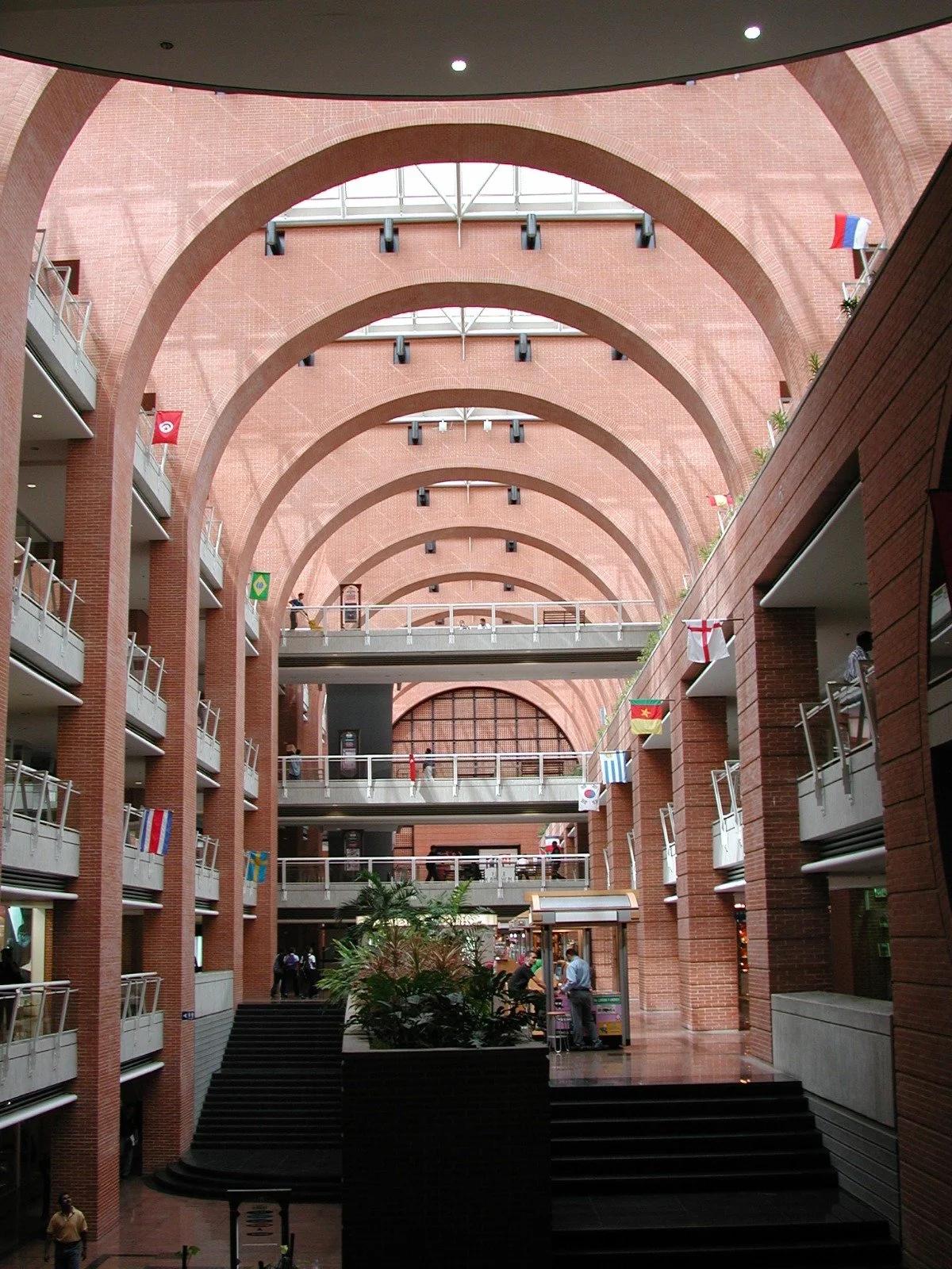 Indoor mall with multiple floors, brick arches, and flags of various countries hanging from balconies.