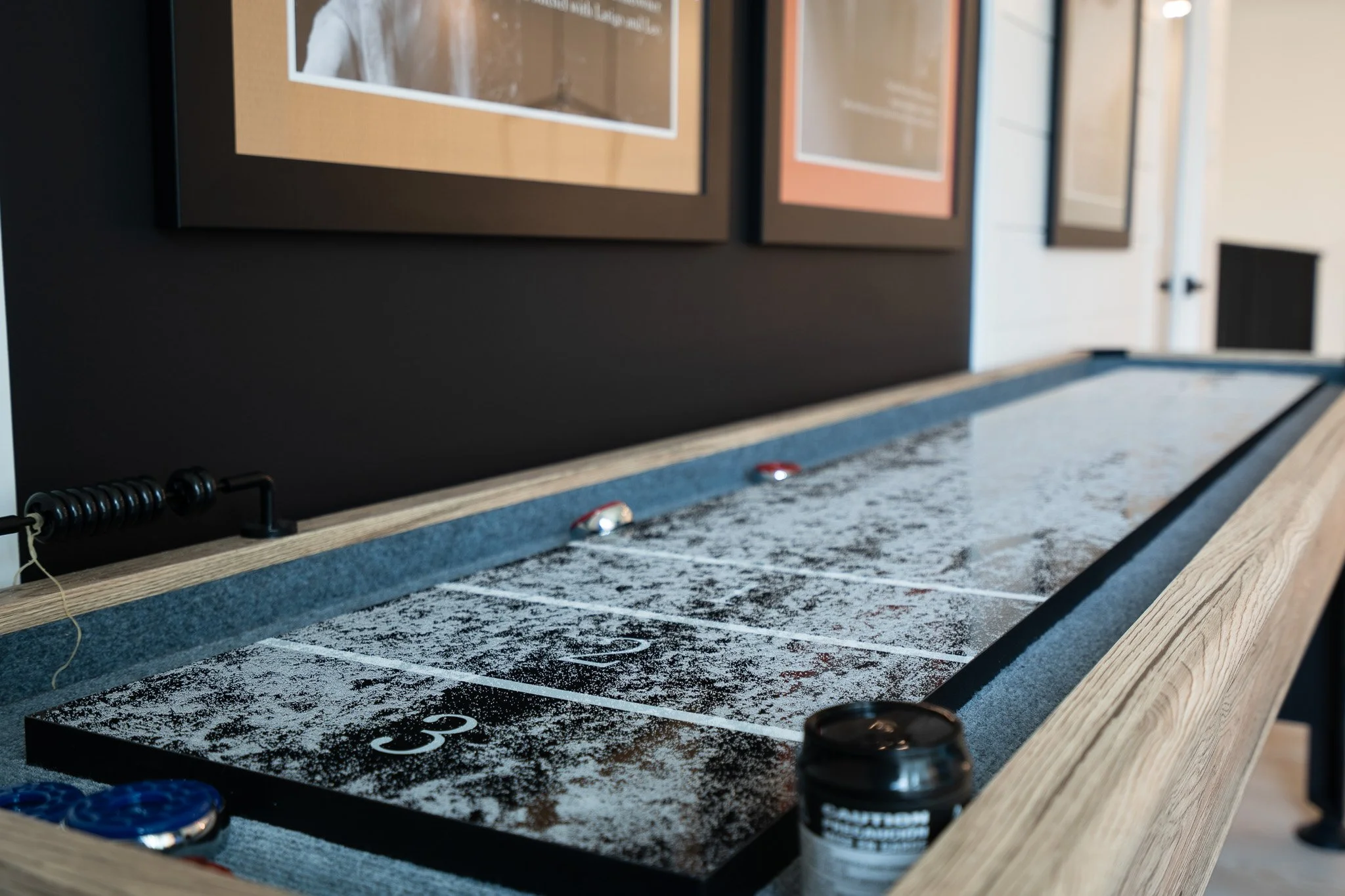 A tabletop shuffleboard game with numbered scoring zones, some black stones, and a glossy black bottle labeled 'SPA' in front of the game.