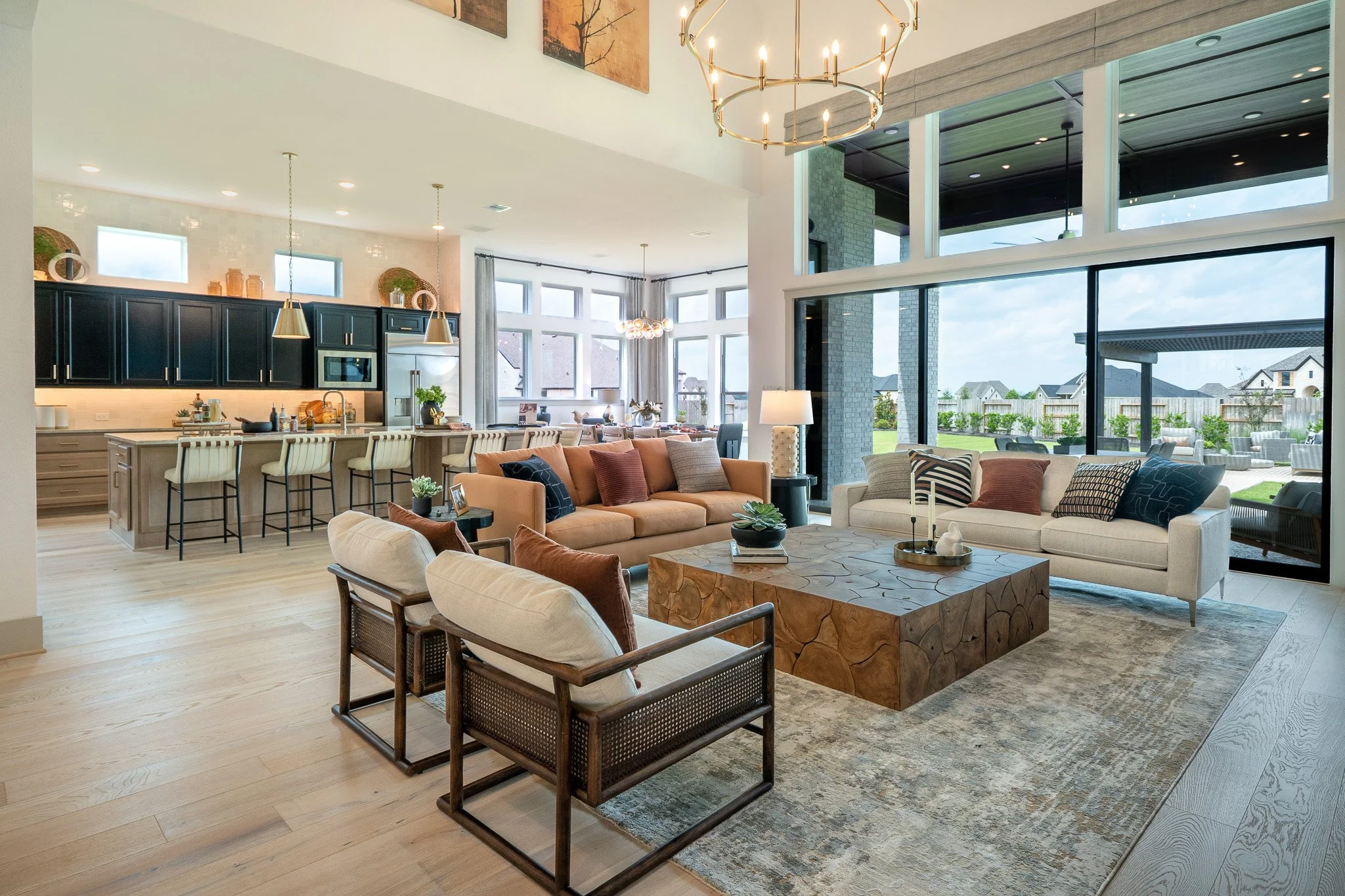 Open-concept living room and kitchen with large windows, modern furniture, and a large chandelier.