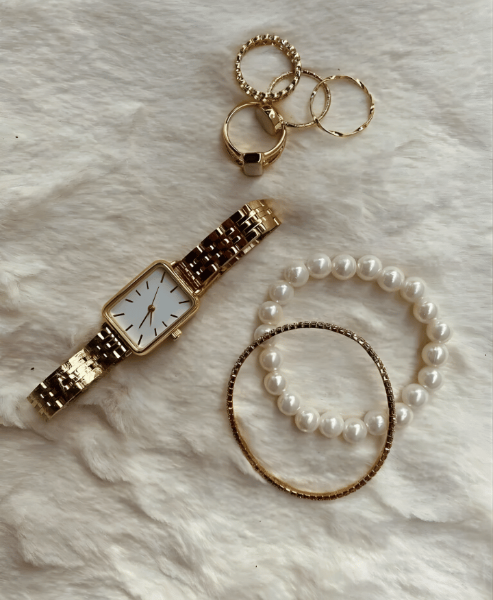 Gold wristwatch with pearl bracelet and gold rings on soft white background