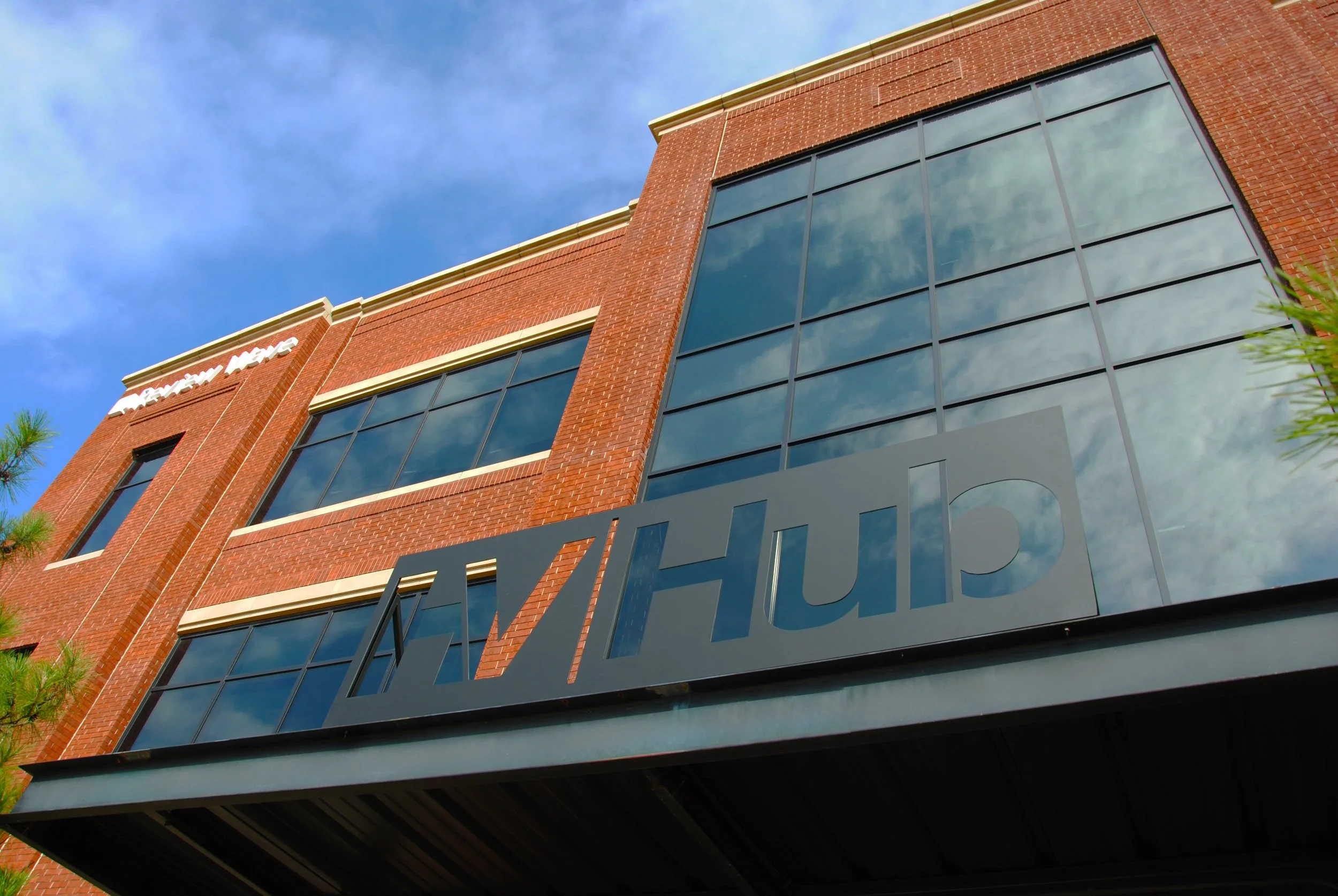 Exterior view of a modern brick building with large reflective glass windows and a metal sign that reads 'CHIP' underneath, with clouds reflected in the windows.