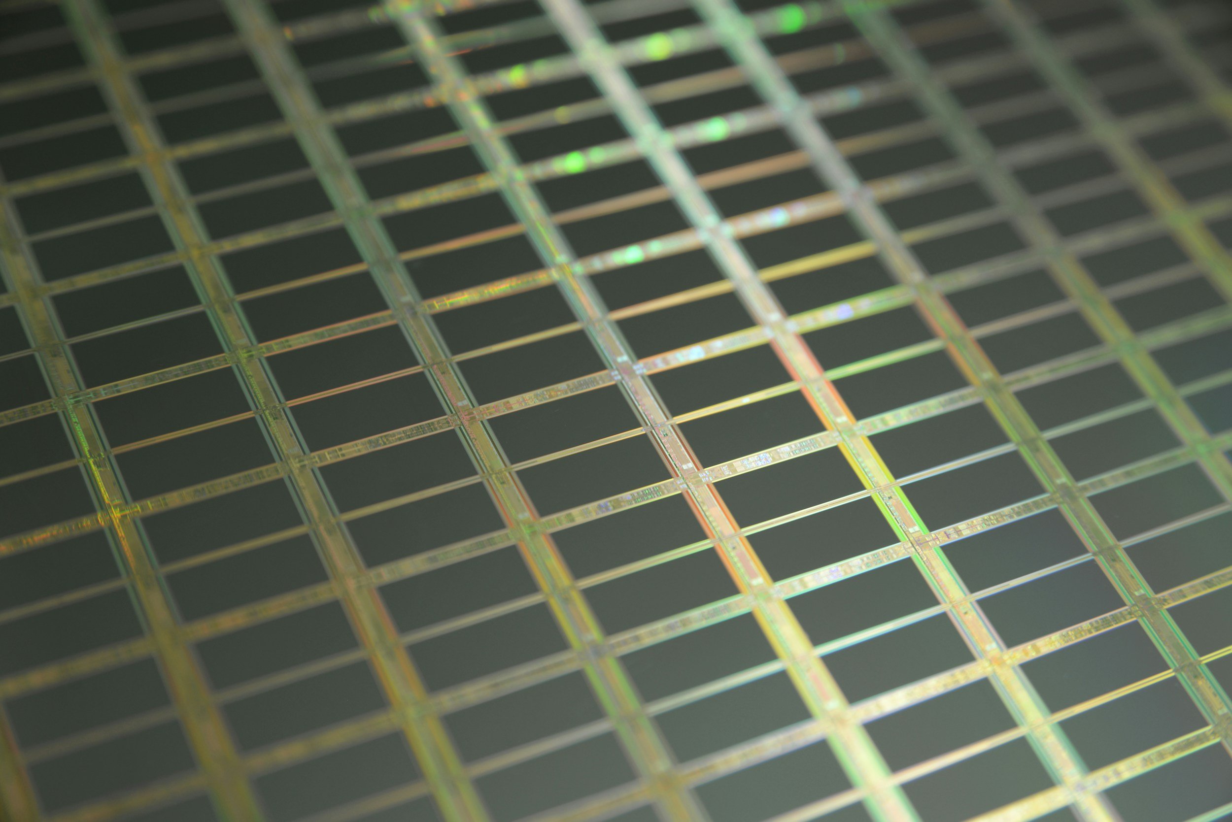Close-up of a silicon wafer with intricate microcircuit patterns and rainbow coloring.
