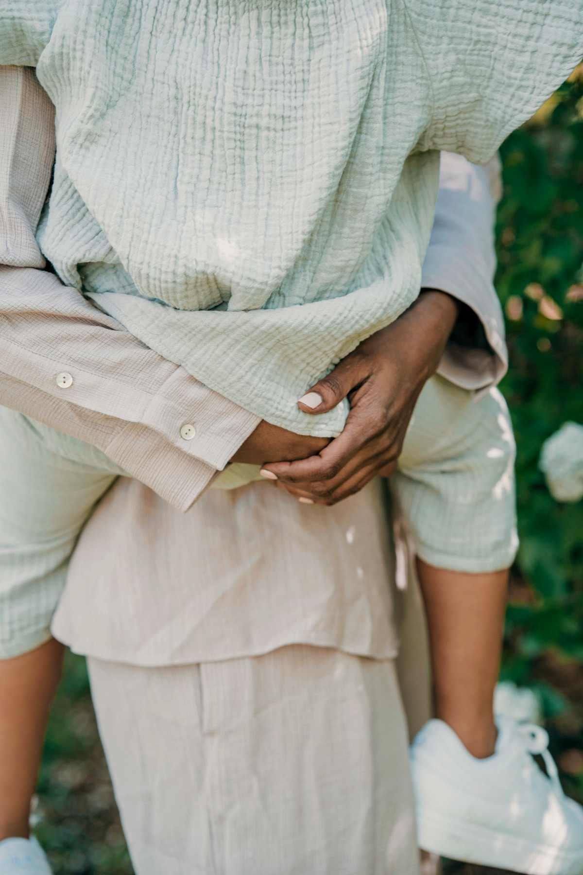 Close-up of a mother carrying a child on their back outdoors in SF Bay Area, with both wearing light-colored clothing.
