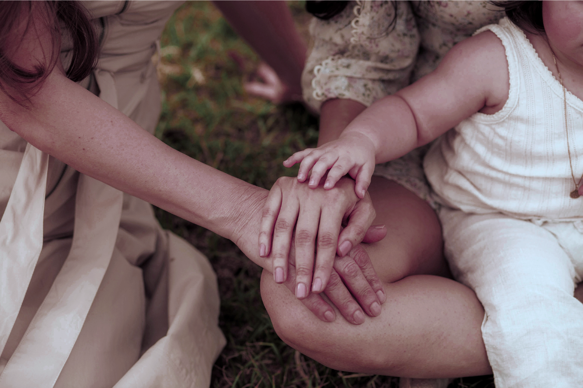 Multiple people, including children, holding hands in a circle outdoors in San Francisco Bay Area.