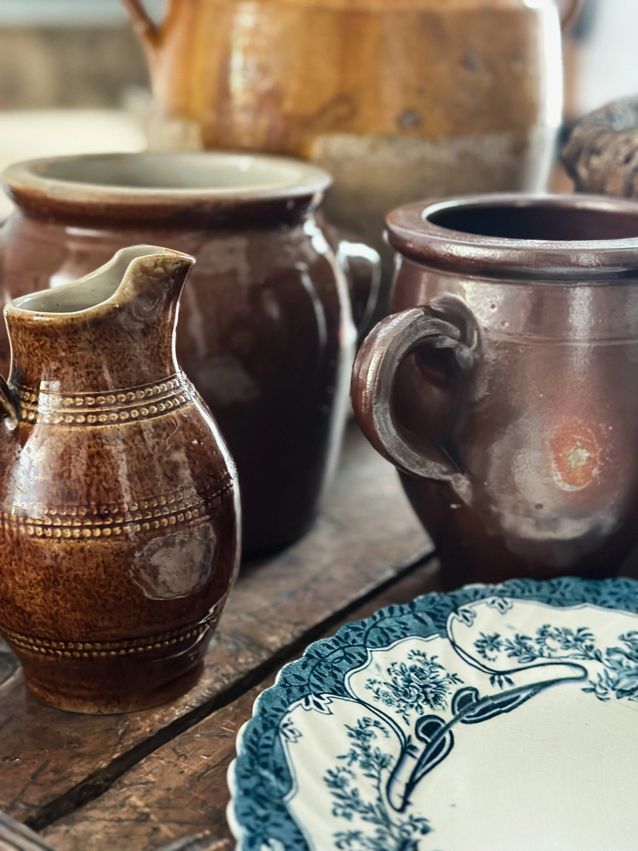 Various brown ceramic pots and dishes on a wooden surface, with a decorative blue and white plate in the foreground.