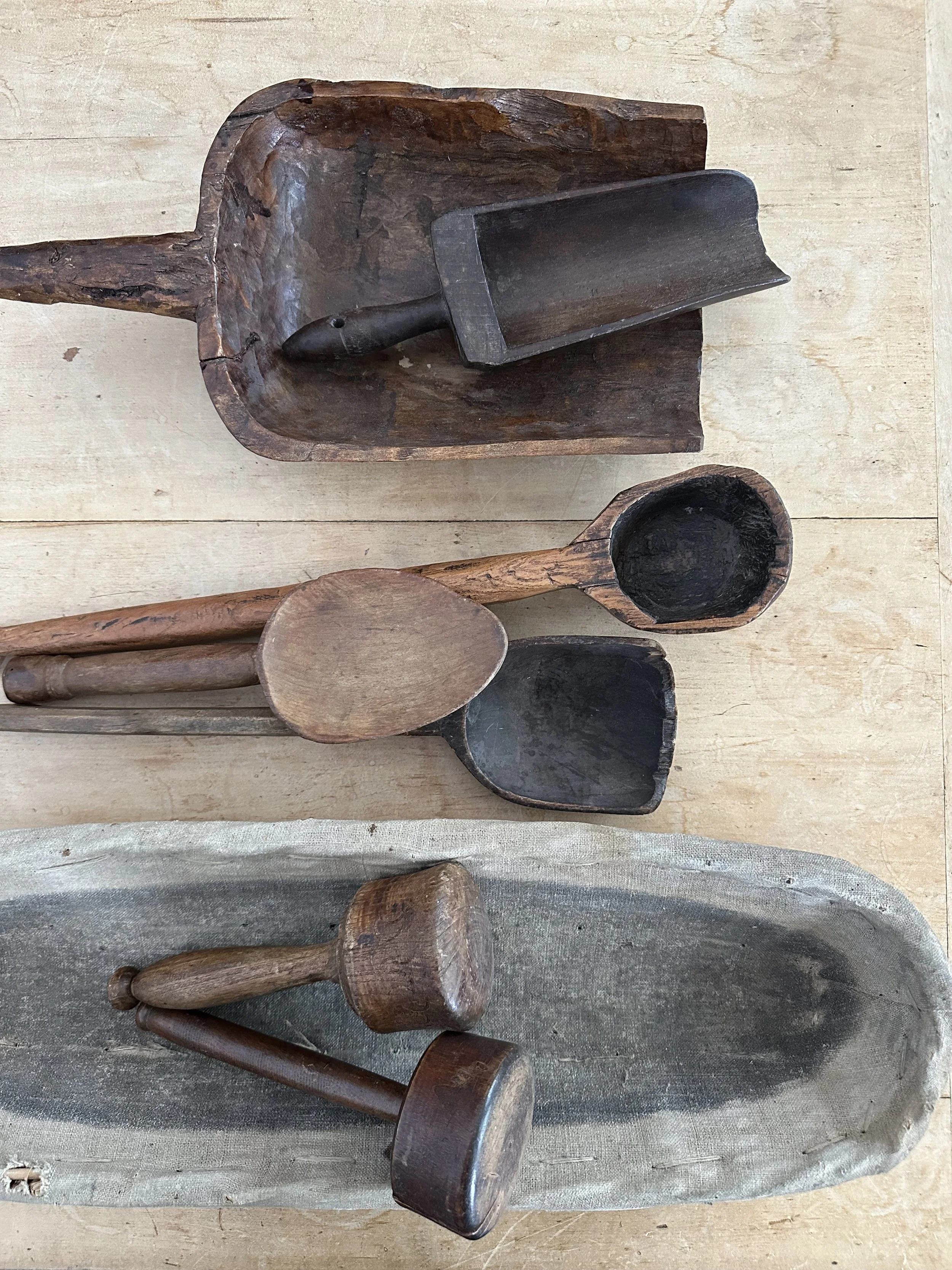 Collection of old wooden toy tools including a scoop, a shovel, a fork, a hammer, and a rolling pin, displayed on a light wooden surface.