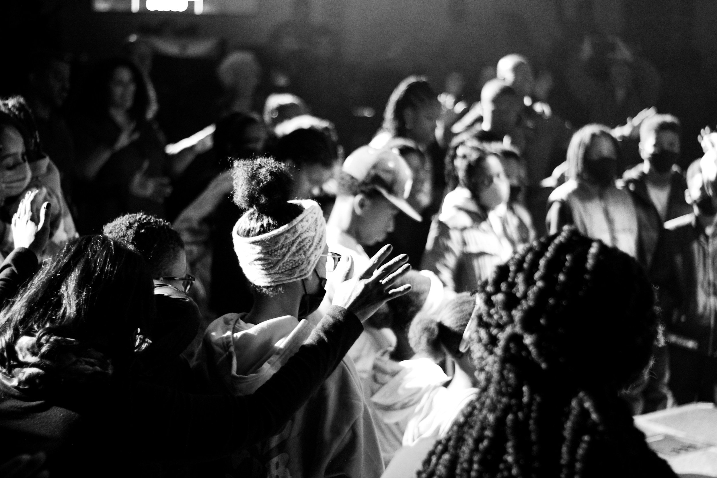 A black-and-white photo of a group of people with some raising their hands in a worship gathering or prayer.