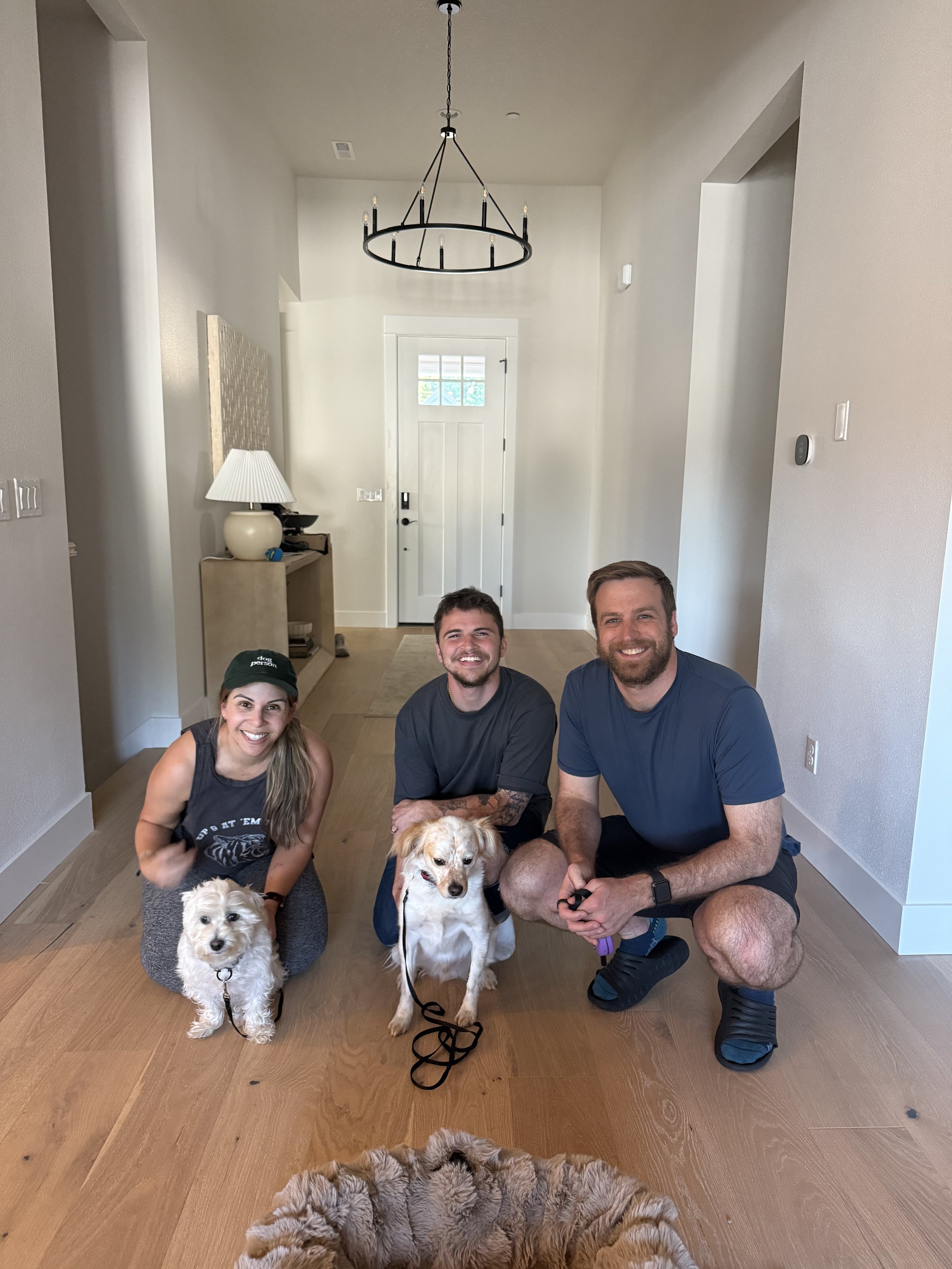 Three people and three dogs posing inside a house, smiling at the camera.