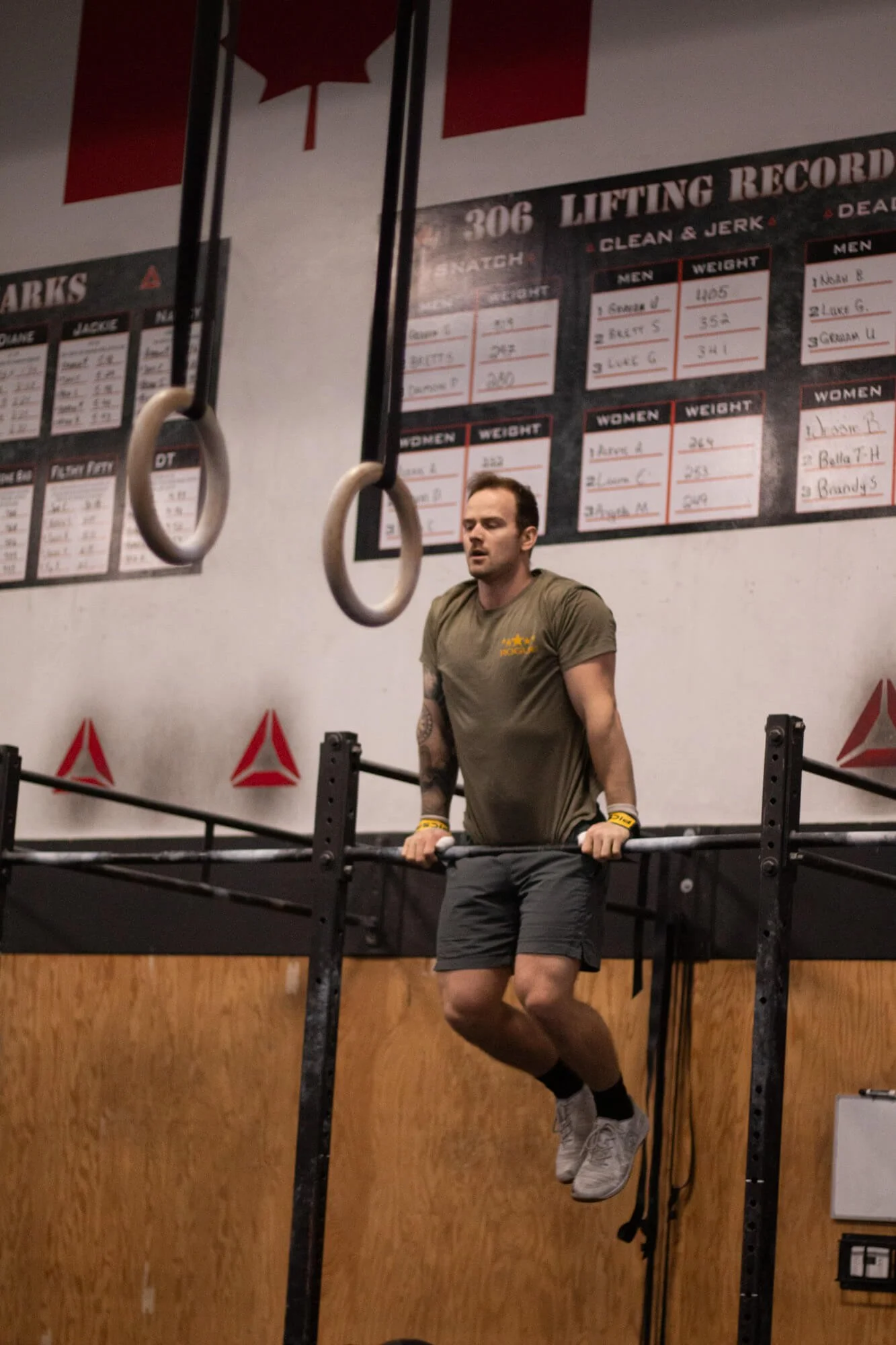 A man performing a dip exercise on gym bars inside a gym, with instructional posters on the wall behind him.