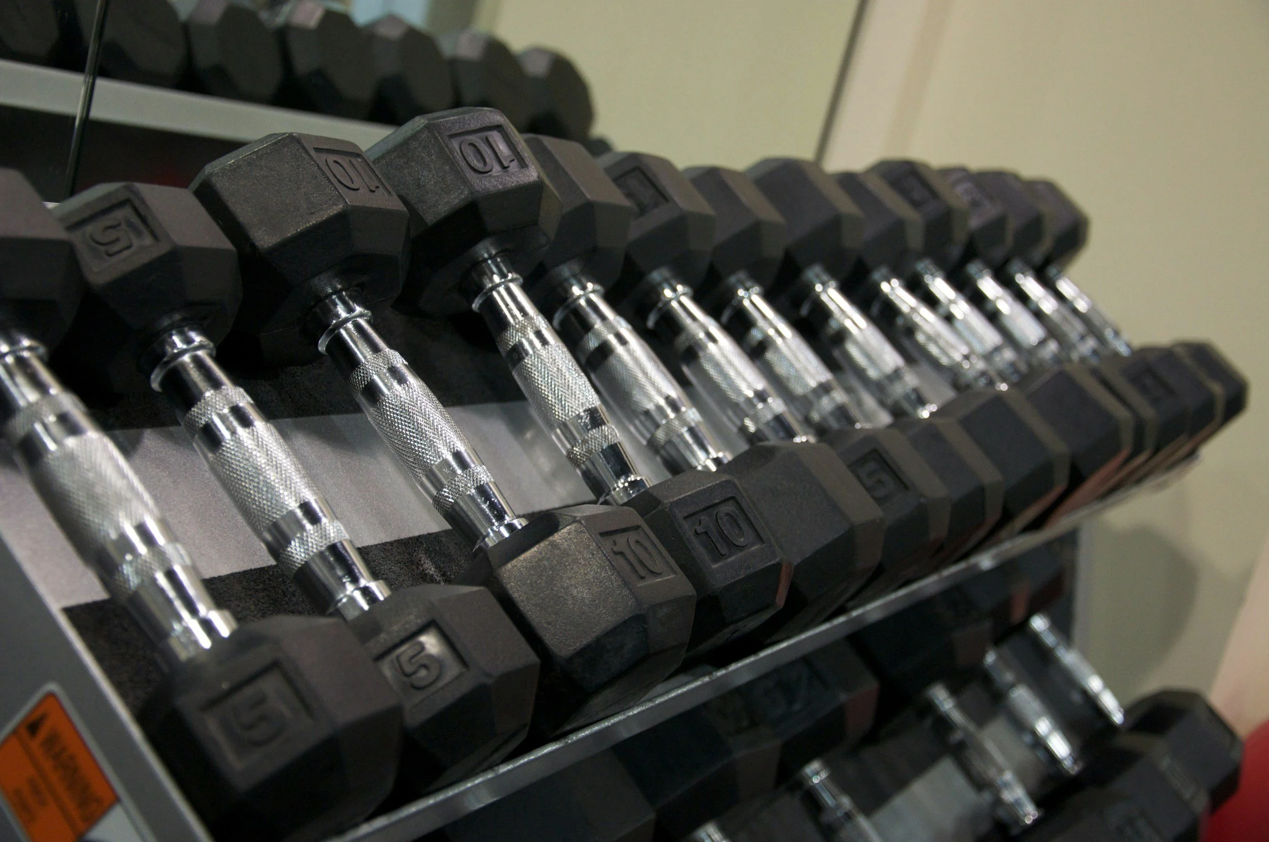 A row of black and silver dumbbells arranged on a rack, with visible weights labeled from 5 to 10 pounds.
