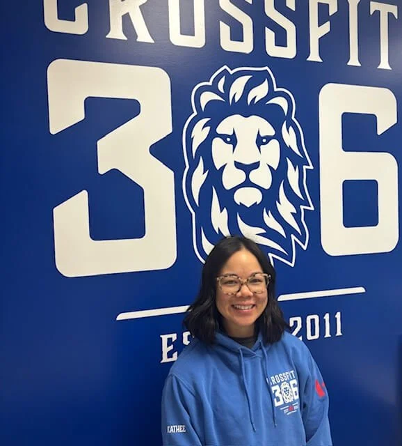 Woman smiling in front of a blue wall with the Crossett 36 logo, a lion's face, and the year 2011, wearing a blue hoodie with the same logo.