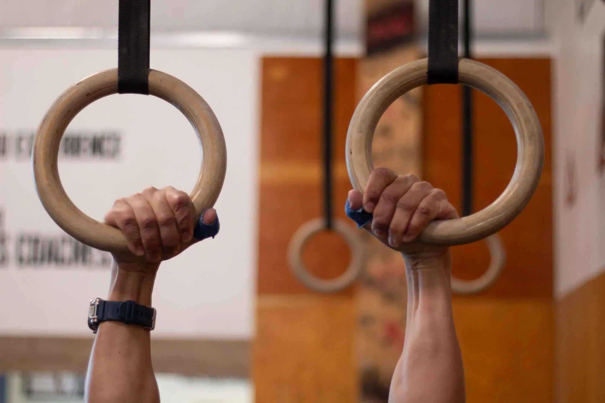 Close-up of two individuals' hands gripping gymnastic rings hanging from black straps in a fitness gym or studio.