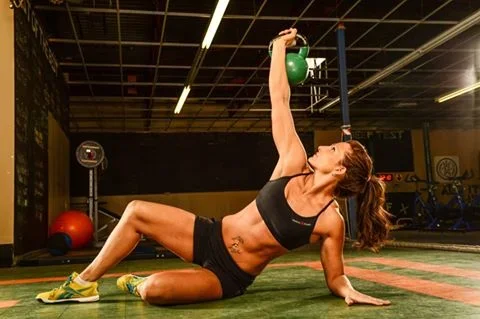 Woman in black sports bra and shorts performing a kettlebell exercise on gym floor