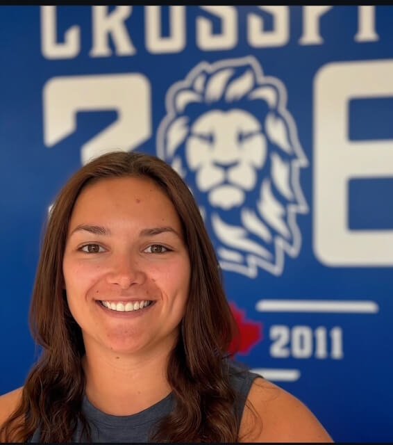 A young woman with long brown hair taking a selfie in front of a blue wall with the 306 Training Grounds logo behind her.