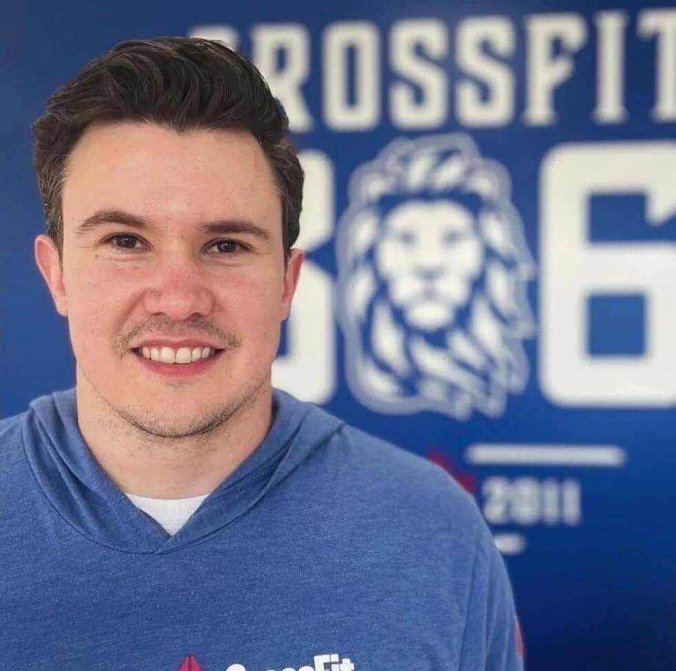 Young man smiling in front of a blue background with a lion logo for the CrossFit 306 training grounds