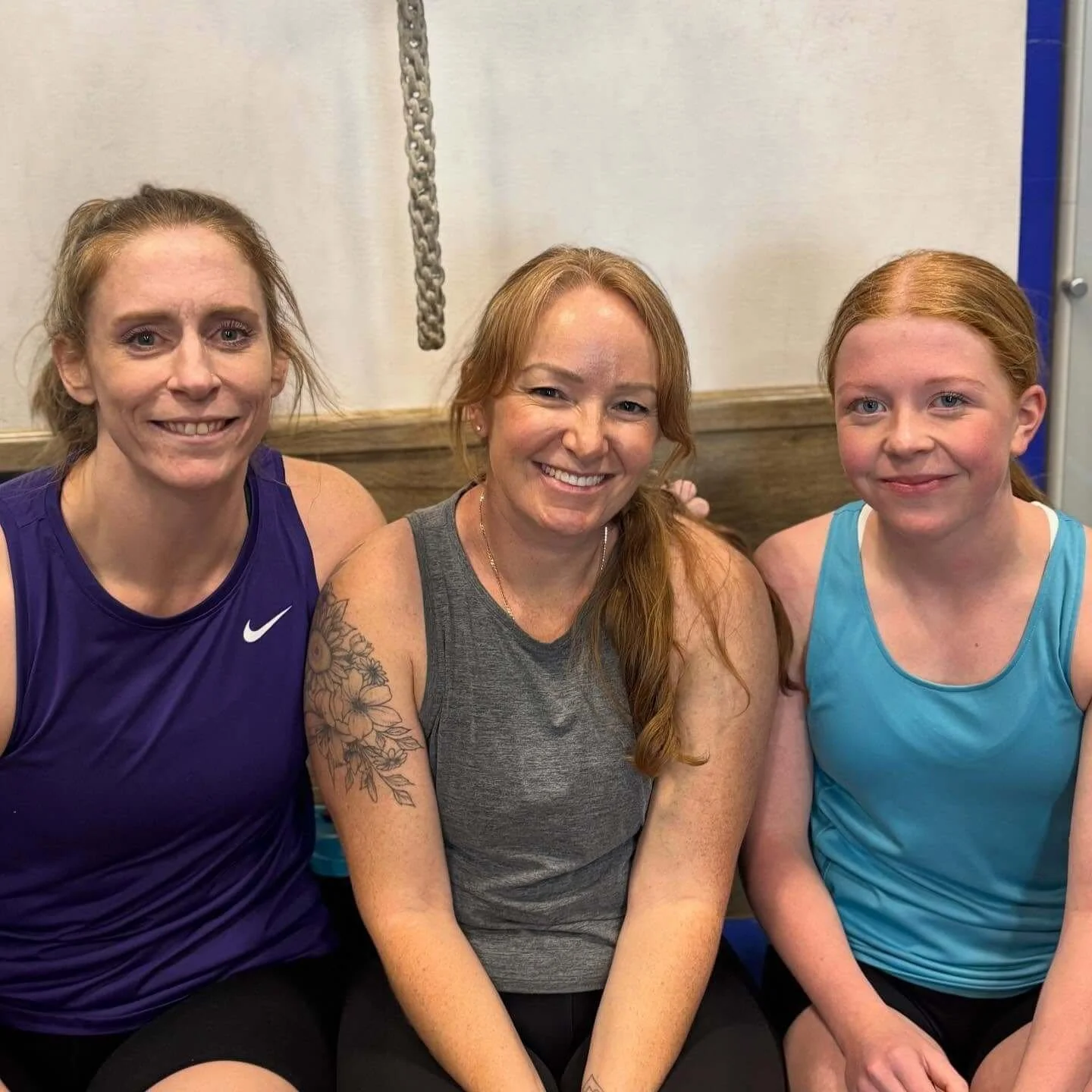 Three women sitting together smiling in a gym or fitness setting.