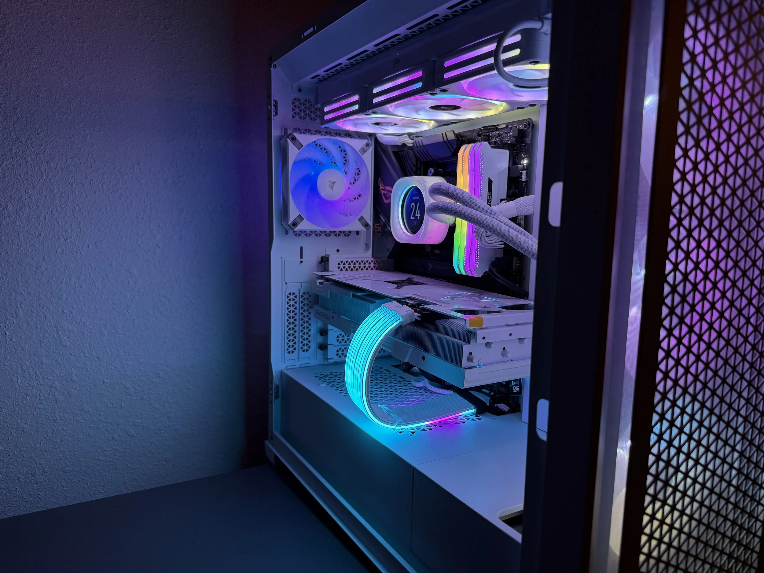 A gaming computer with RGB lighting inside a white case, featuring a cooling fan, RAM sticks with RGB lights, a graphics card, and white cables with RGB accents.